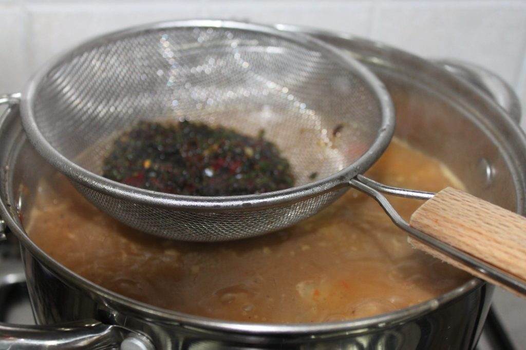 Extrayendo el jugo del pimiento choricero con un colador y cuchara sobre la cazuela de fideos