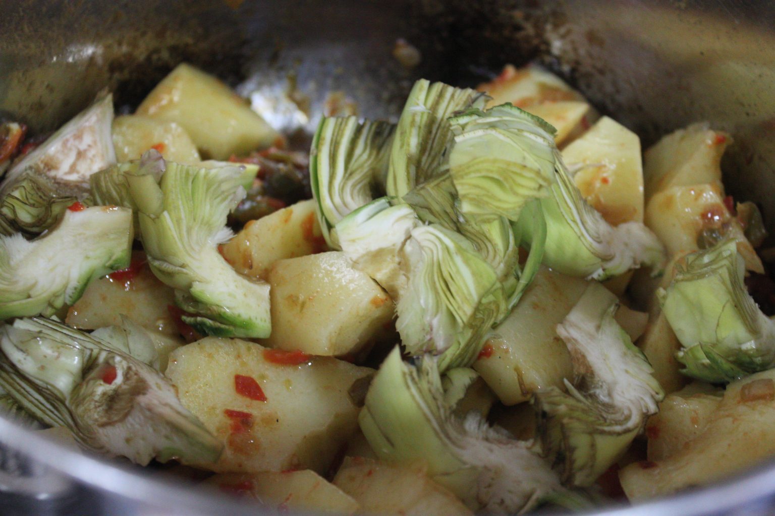 Añadiendo corazones de alcachofas y patatas a cuartos al sofrito de verduras
