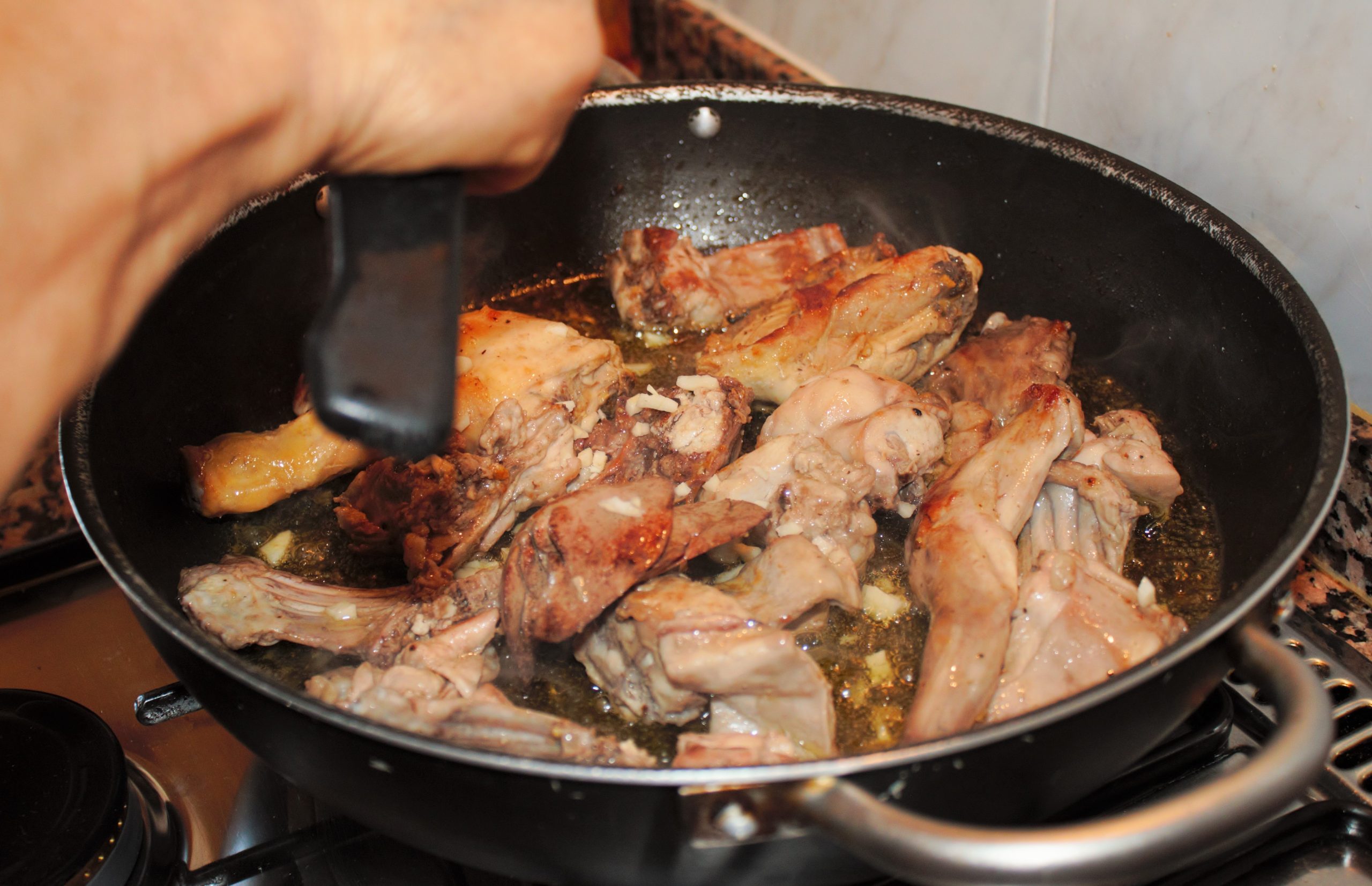 Añadiendo ajo picado al conejo dorado en la paella