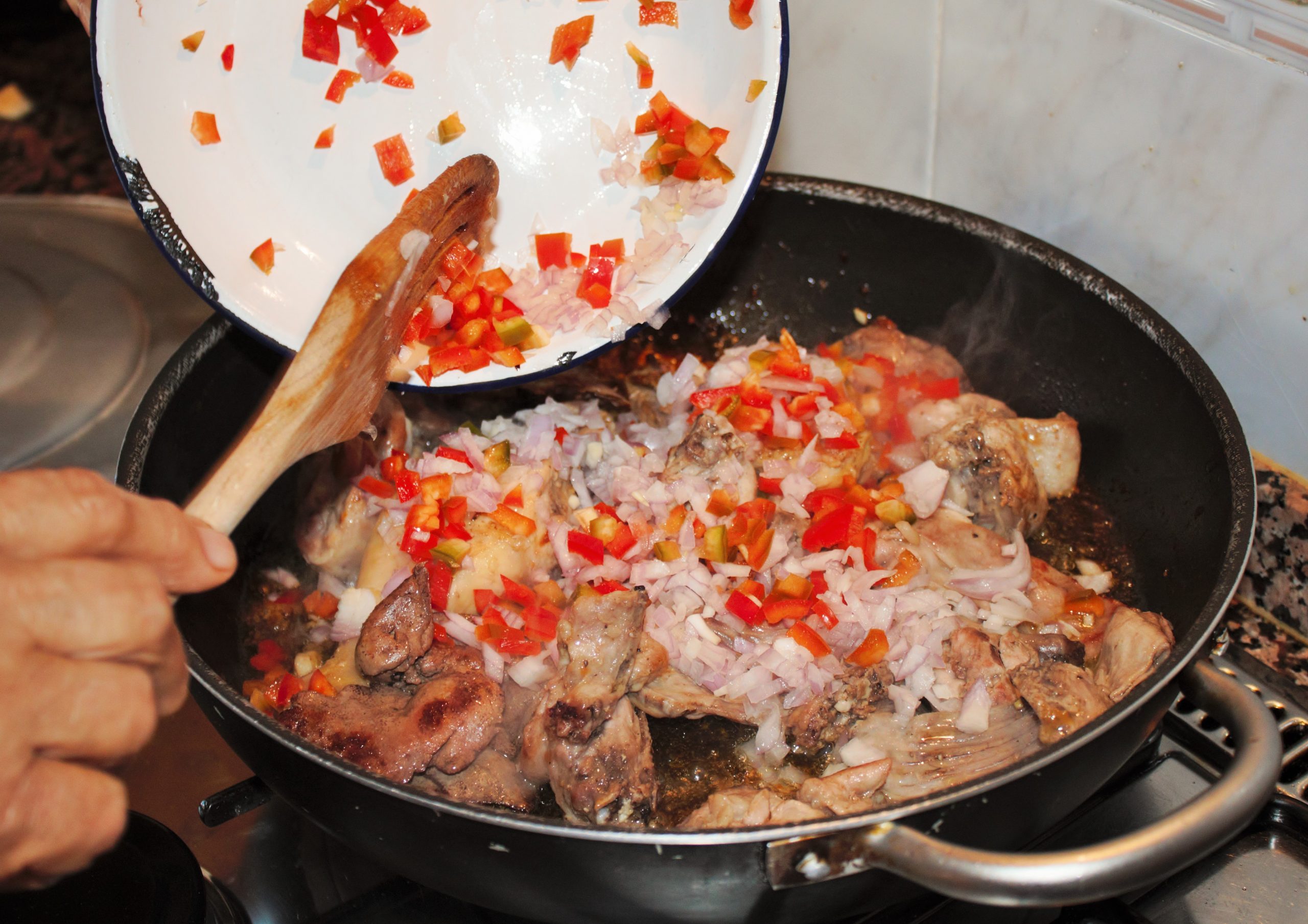 Añadiendo la cebolla al conejo dorado en la paella