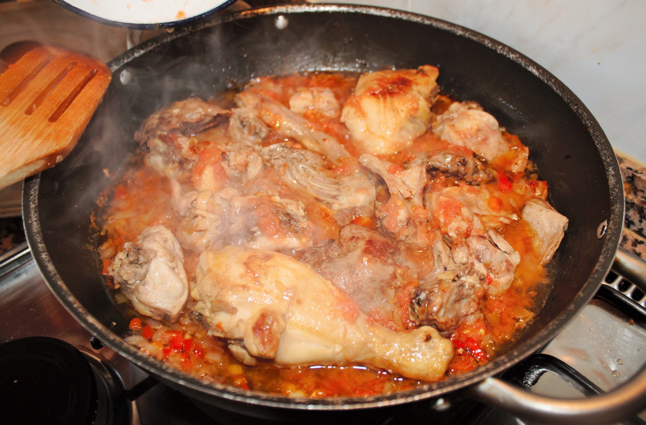 Añadiendo tomate triturado al sofrito de conejo para crear la base del arroz
