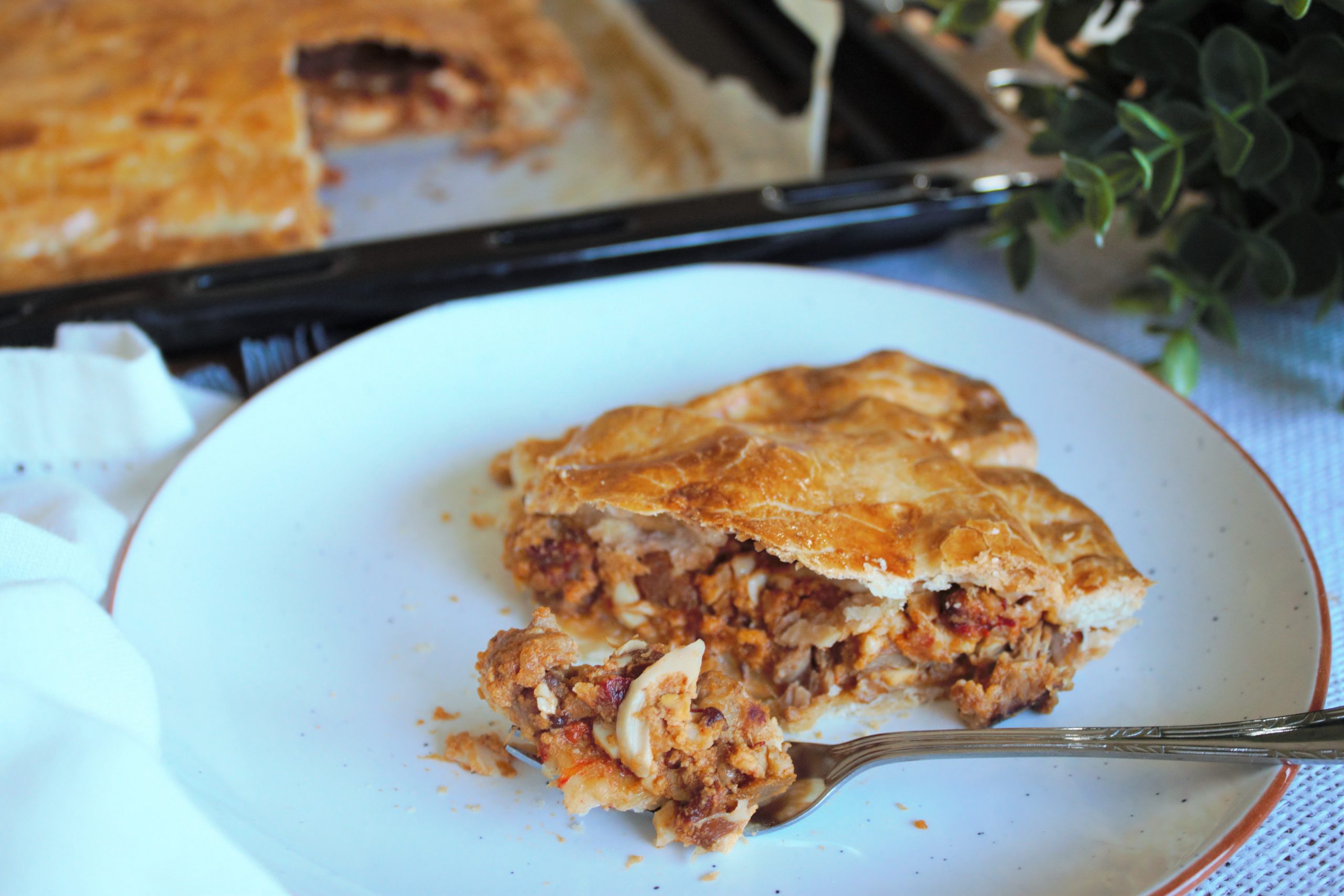 Empanada casera dorada y brillante rellena de carne de cerdo y pimientos asados, recién horneada sobre papel vegetal."