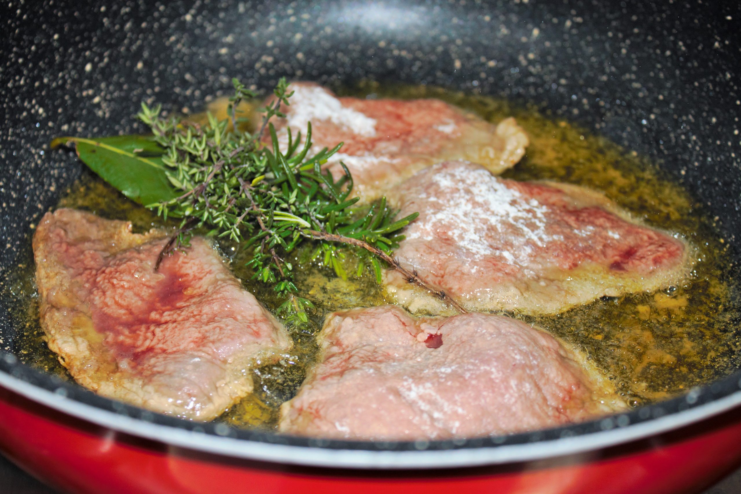 Sellado de la carne de ternera en una cazuela con aceite caliente y un atadillo de hierbas aromáticas.