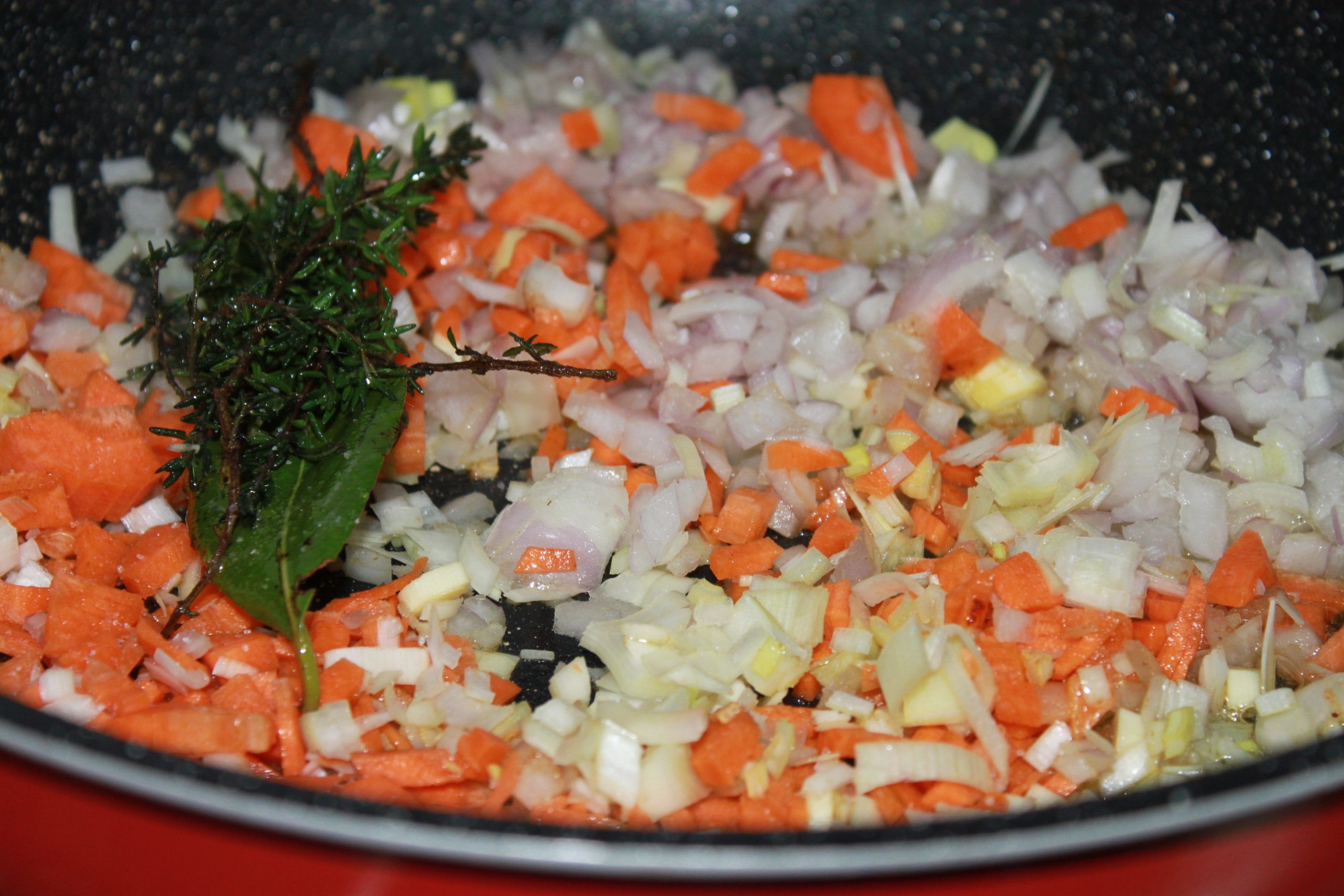 Sofrito de cebolla, zanahoria, puerro y ajo pochándose lentamente en la cazuela.