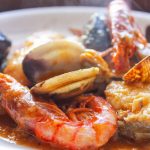 Zarzuela de pescado brillante y melosa reposando en la cazuela, con las almejas y mejillones abiertos en su punto.