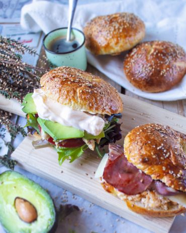 Bagel casero recién horneado con semillas de sésamo y amapola sobre una superficie de madera rústica, luz natural suave y ambiente cálido de cocina.