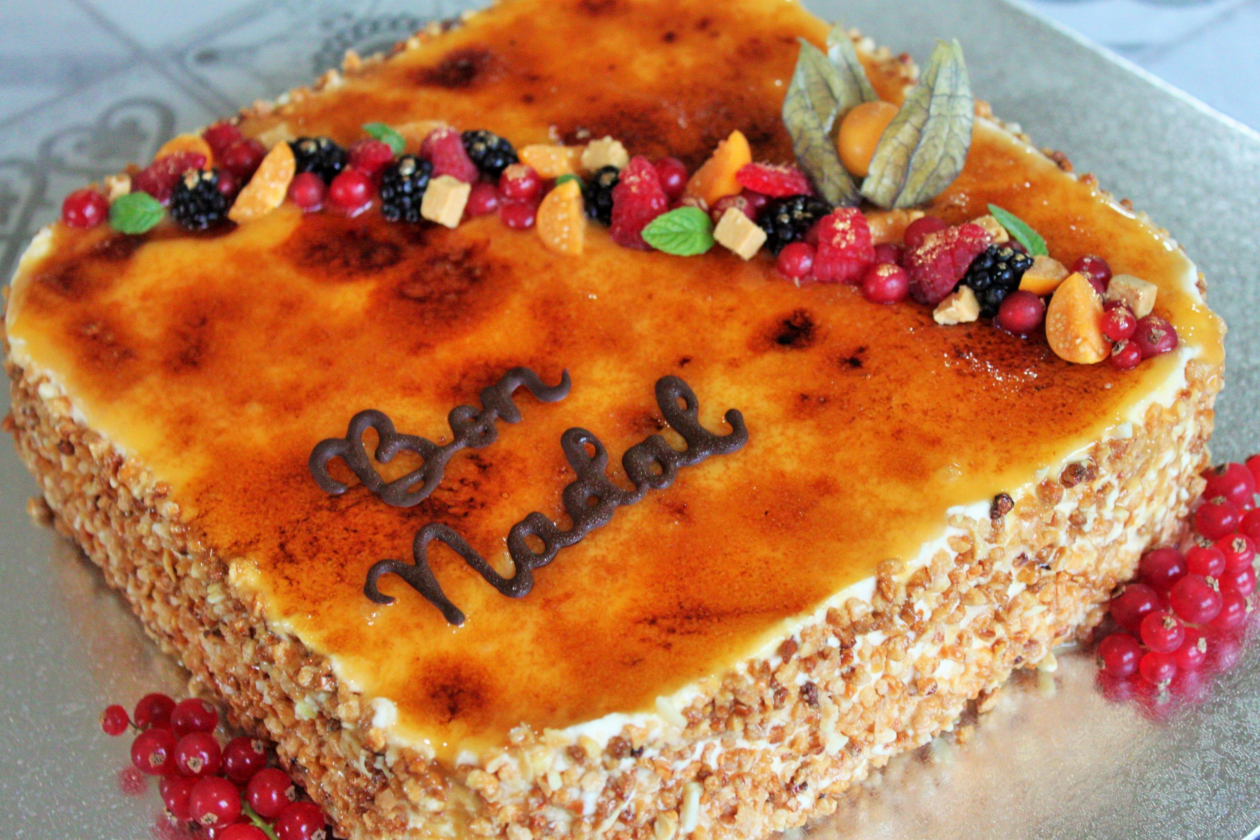 Tarta artesana de turrón de Jijona con cobertura de yema quemada, decorada con almendras y frutas frescas, estilo pastelería clásica."