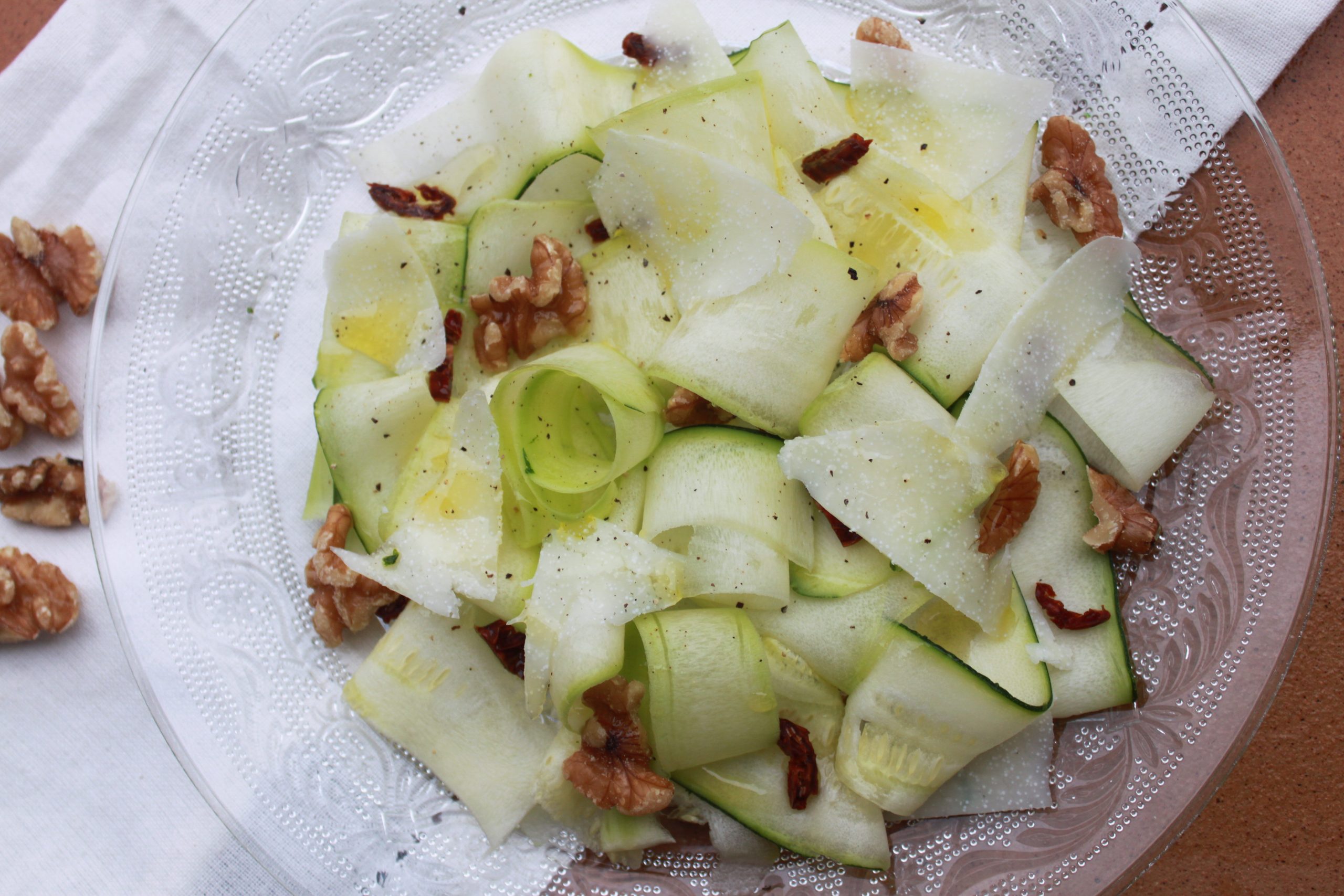 Carpaccio de calabac&iacute;n con tomate seco, nueces y queso de oveja en plato de cer&aacute;mica.