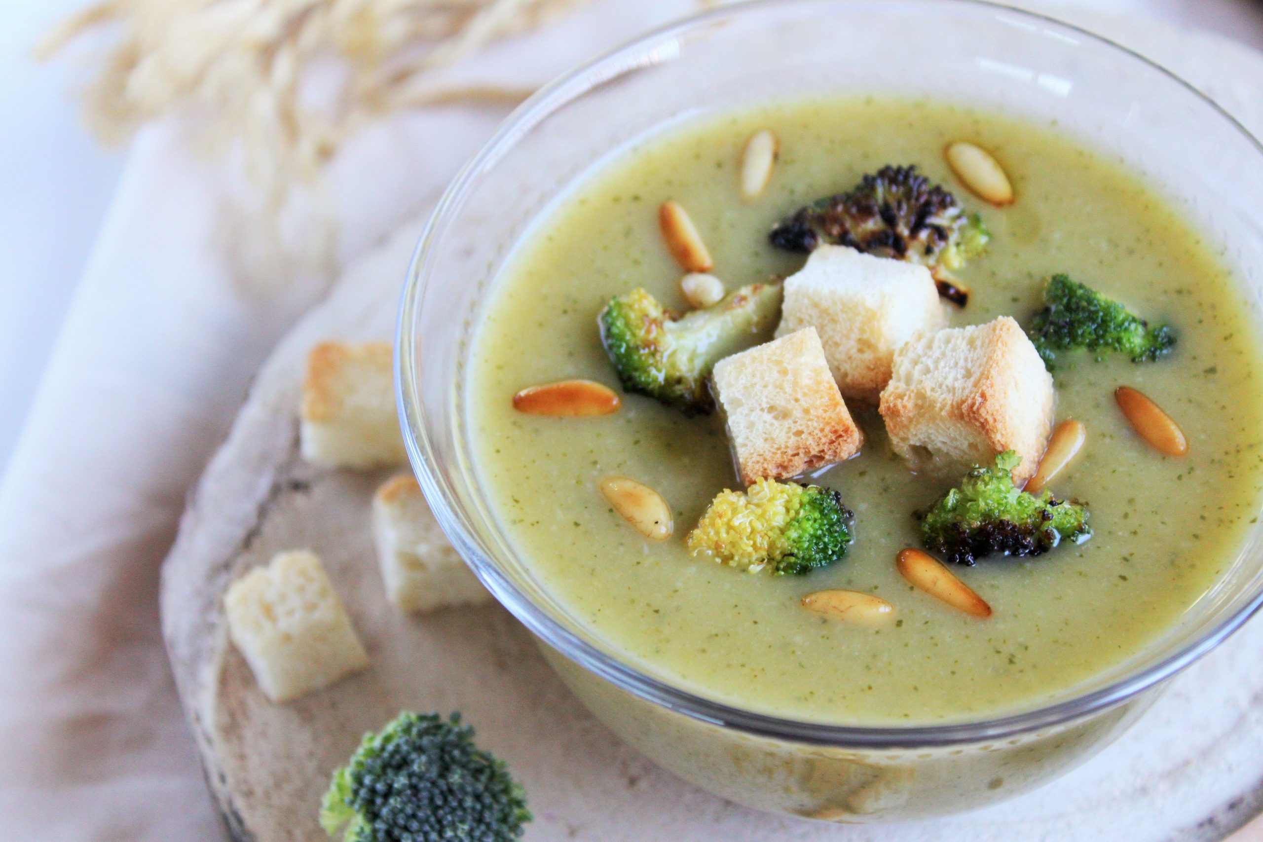 Crema de calabacín blanco y brócoli con queso Havarti derretido, decorada con piñones tostados en un bol de cerámica.