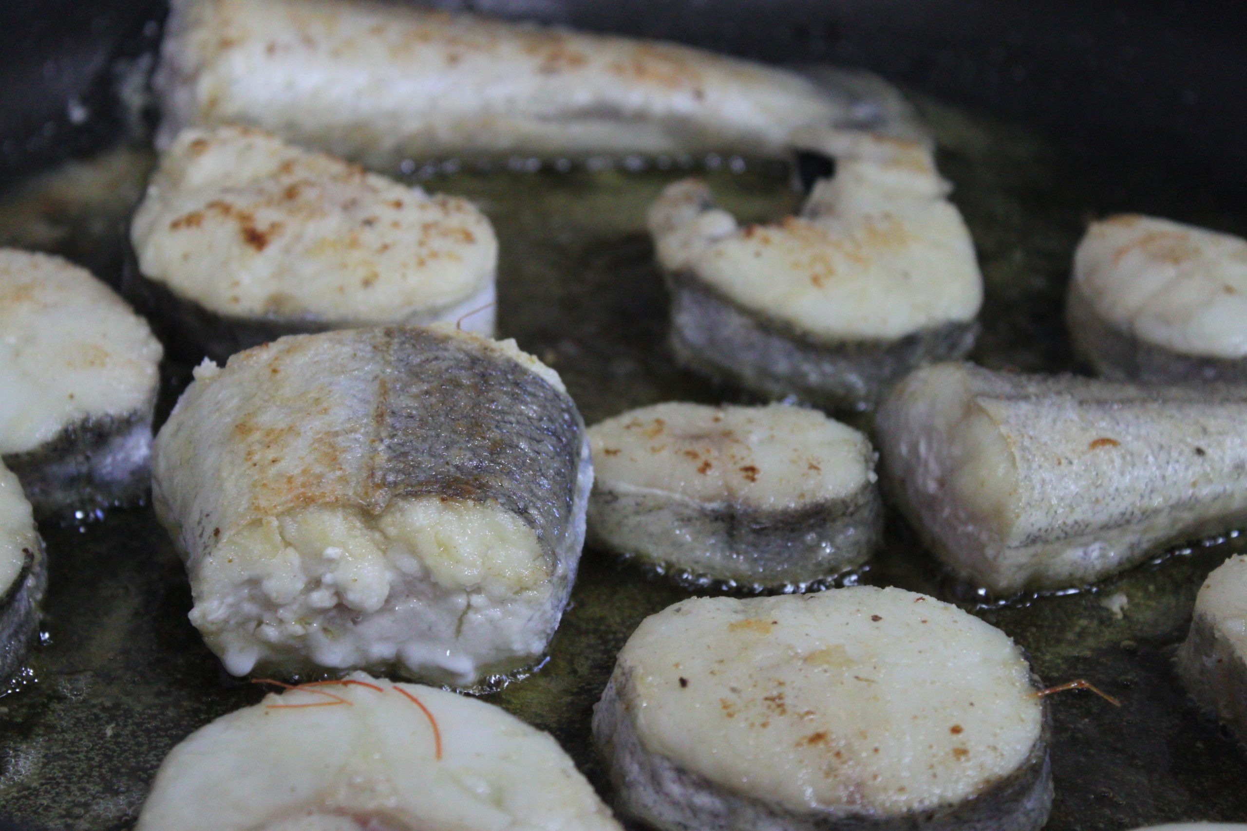 Rodajas de merluza y rape ligeramente enharinadas dorándose en aceite de oliva en cazuela de barro.