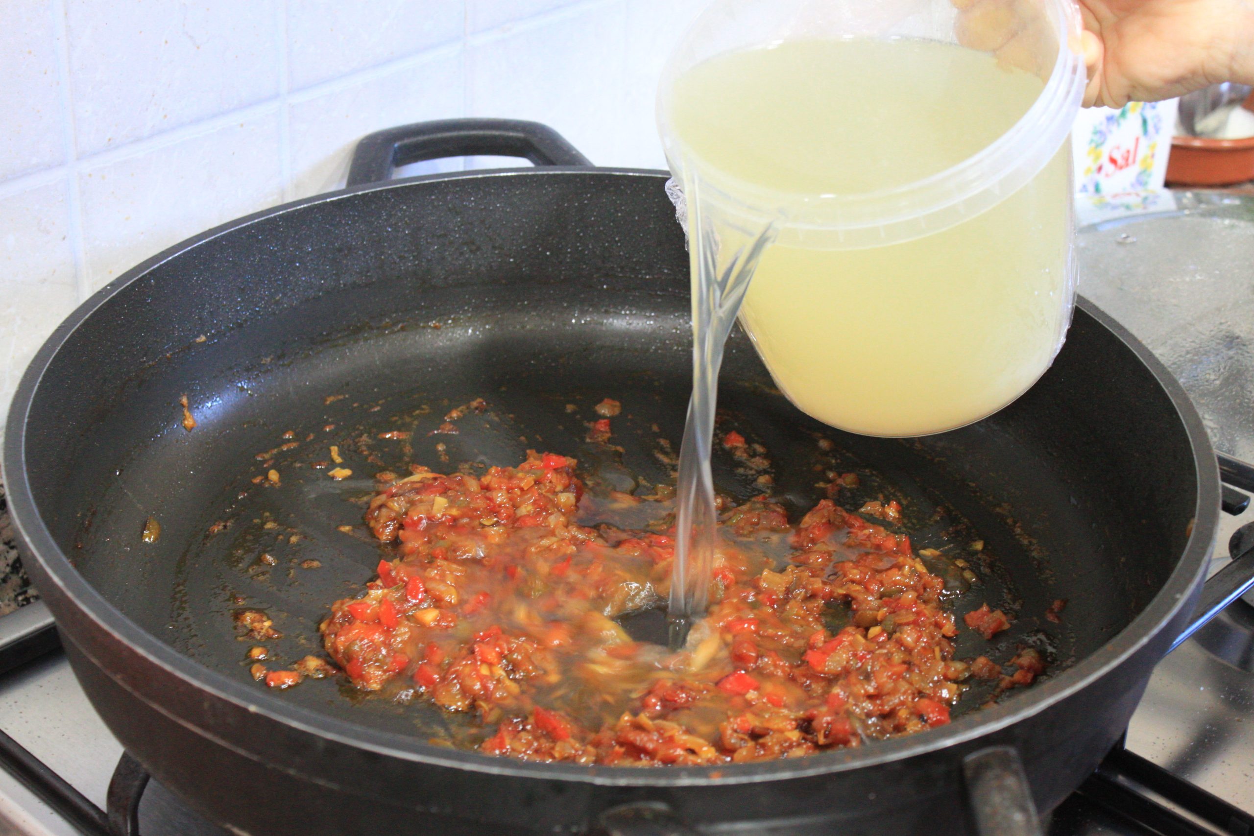 Añadiendo el fumet de pescado en la cazuela con el sofrito de verduras.