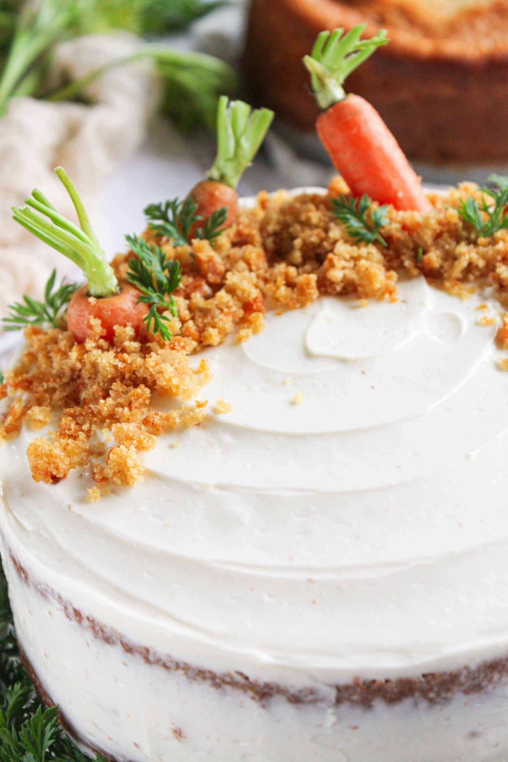 Tarta de zanahoria rústica con cobertura de crema de queso, decorada con zanahorias baby frescas y hojas verdes sobre una mesa de madera blanca rústica