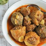 Alcachofas y patatas asadas al horno, rellenas y gratinadas, servidas en una fuente sobre una mesa de madera.