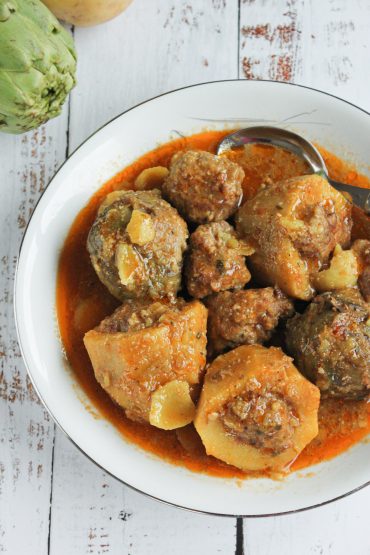 Alcachofas y patatas asadas al horno, rellenas y gratinadas, servidas en una fuente sobre una mesa de madera.