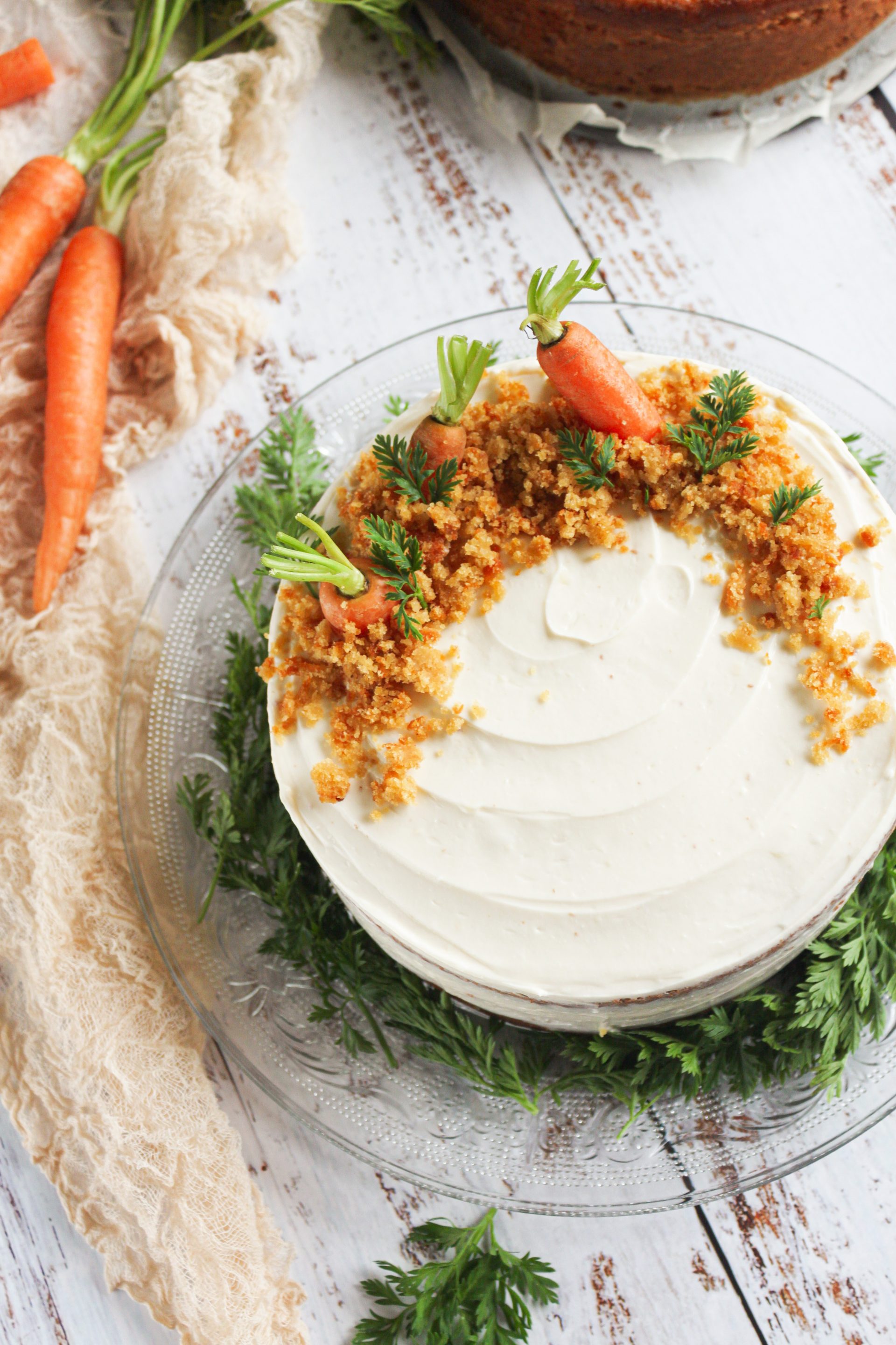 Tarta de zanahoria rústica con cobertura de crema de queso, decorada con zanahorias baby frescas y hojas verdes sobre una mesa de madera blanca rústica