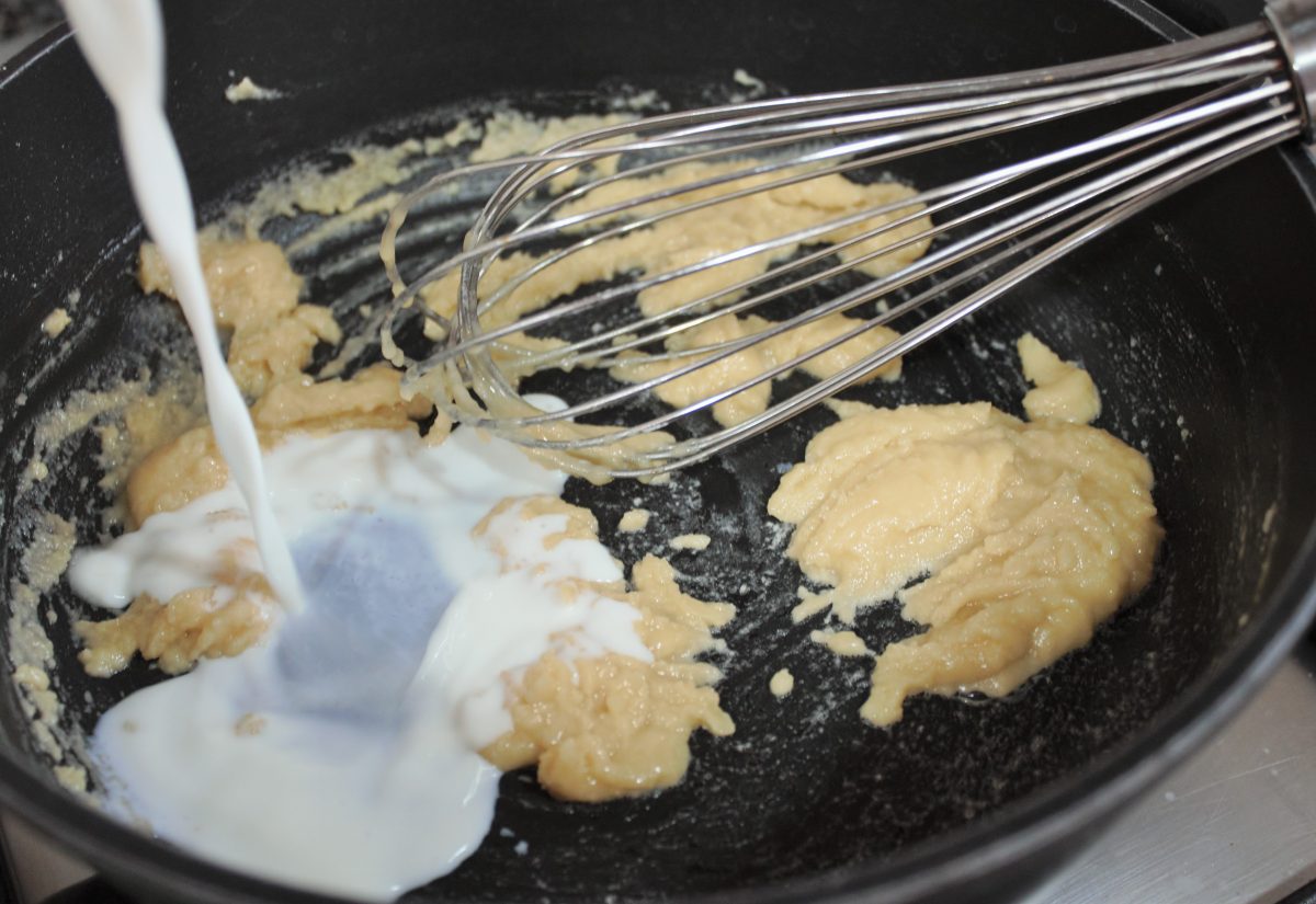 Añadiendo leche templada poco a poco al roux mientras se bate con varillas manuales