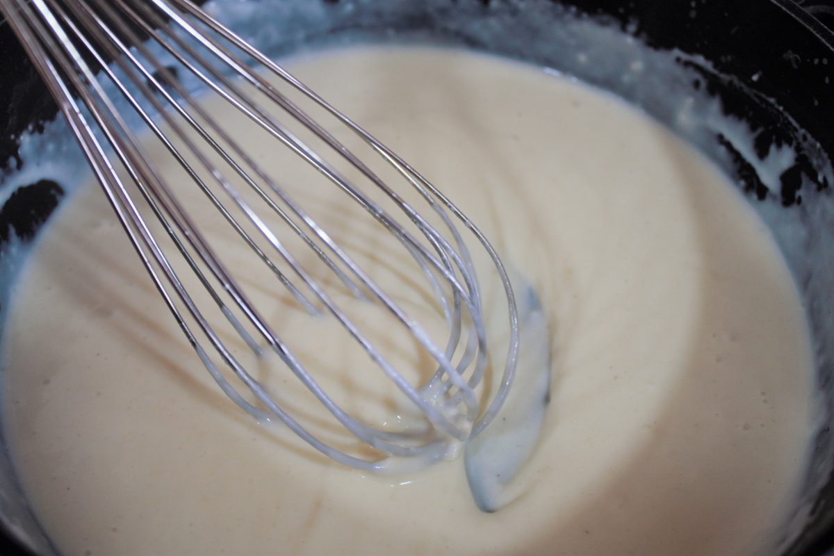 Añadiendo leche templada poco a poco al roux mientras se bate con varillas manuales