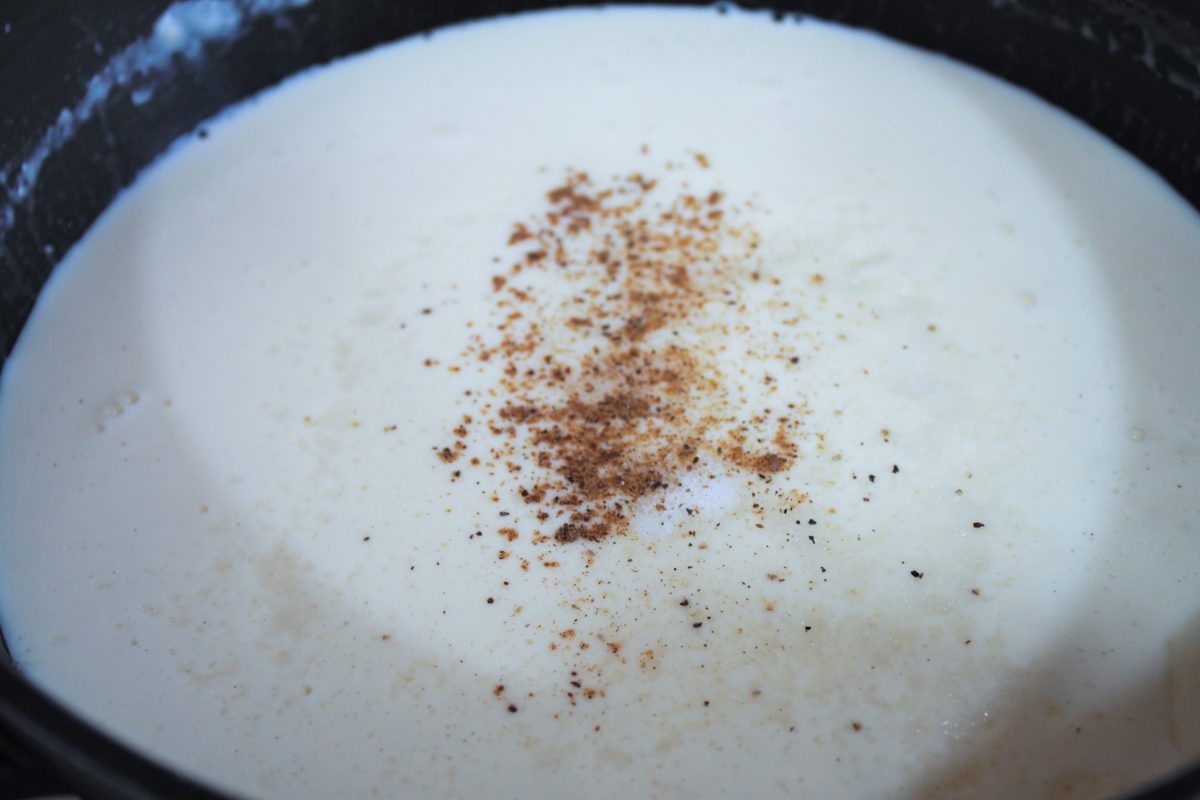Añadiendo nuez moscada rallada y pimienta a la crema bechamel para aromatizar