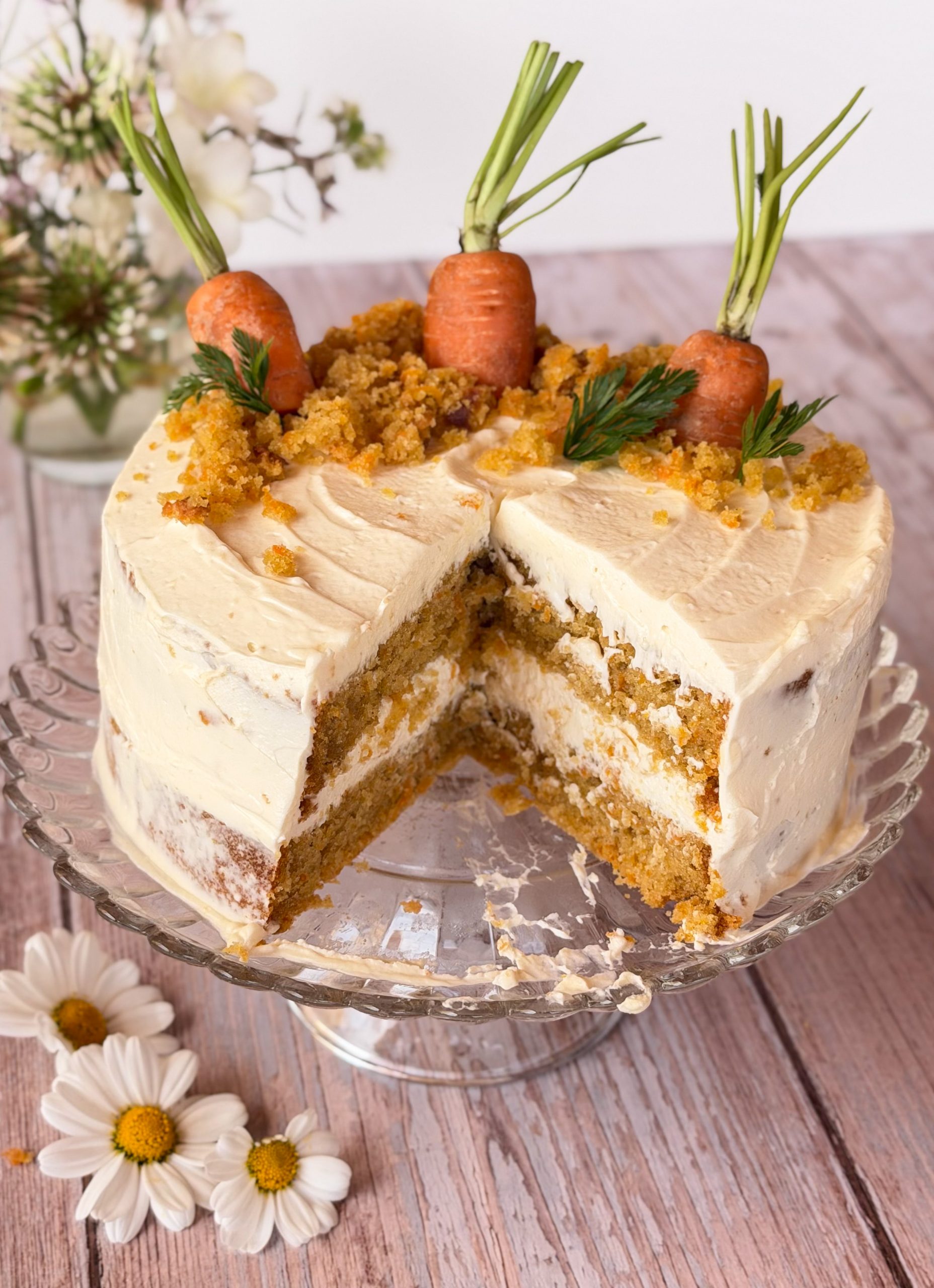 Primer plano del corte de una tarta de zanahoria jugosa showing capas de bizcocho h&uacute;medo y crema de queso, con una zanahoria baby decorativa encima.