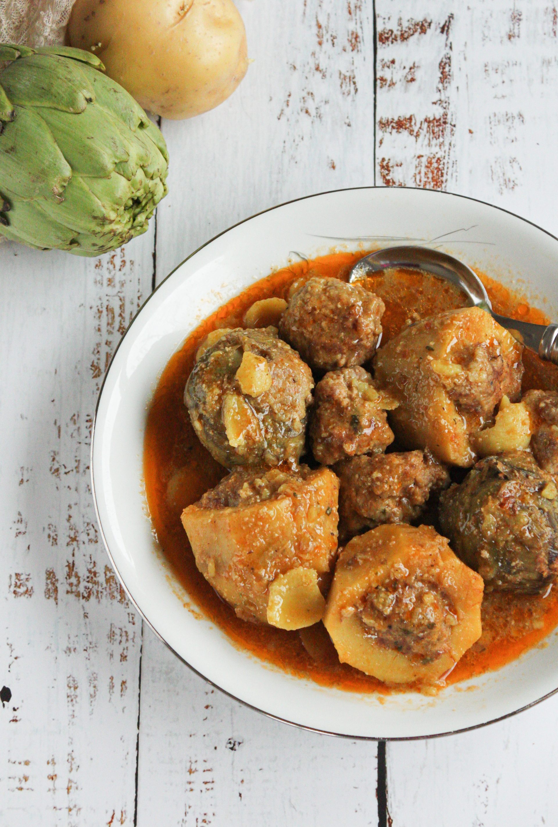 APlato con patatas guisadas al estilo tradicional de Granada, con una salsa trabada de color dorado por el azafrán y las almendras. Ambiente rústico con luz cálida, una cuchara de madera al lado y un paño de lino, transmitiendo la esencia de la cocina Soul Fooding.