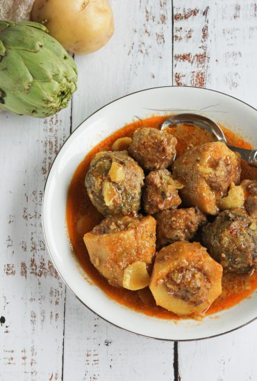Plato con patatas guisadas al estilo tradicional de Granada, con una salsa trabada de color dorado por el azafrán y las almendras. Ambiente rústico con luz cálida, una cuchara de madera al lado y un paño de lino, transmitiendo la esencia de la cocina Soul Fooding.