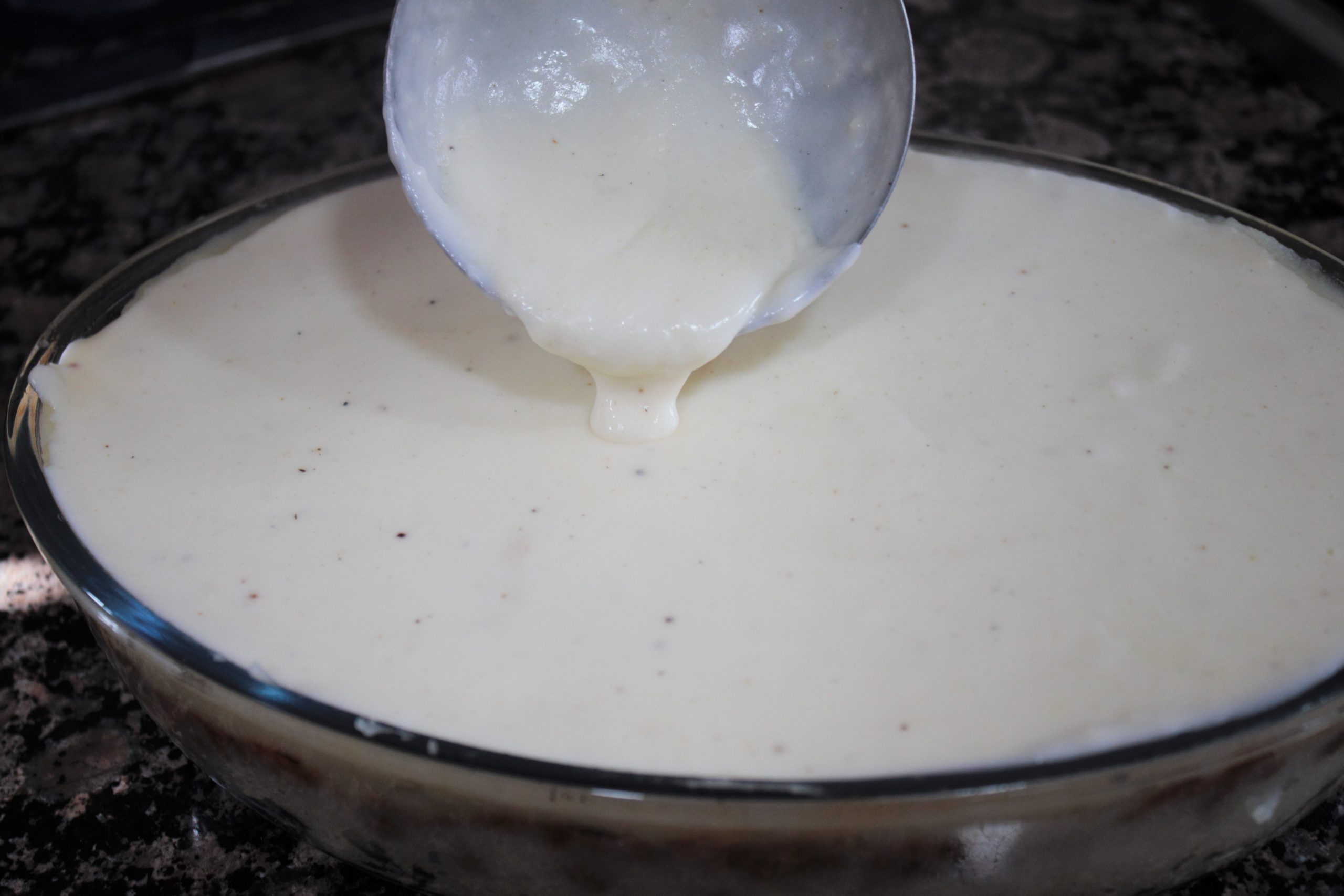 Capa de bechamel y queso emmental rallado sobre pastel de patata antes de hornear