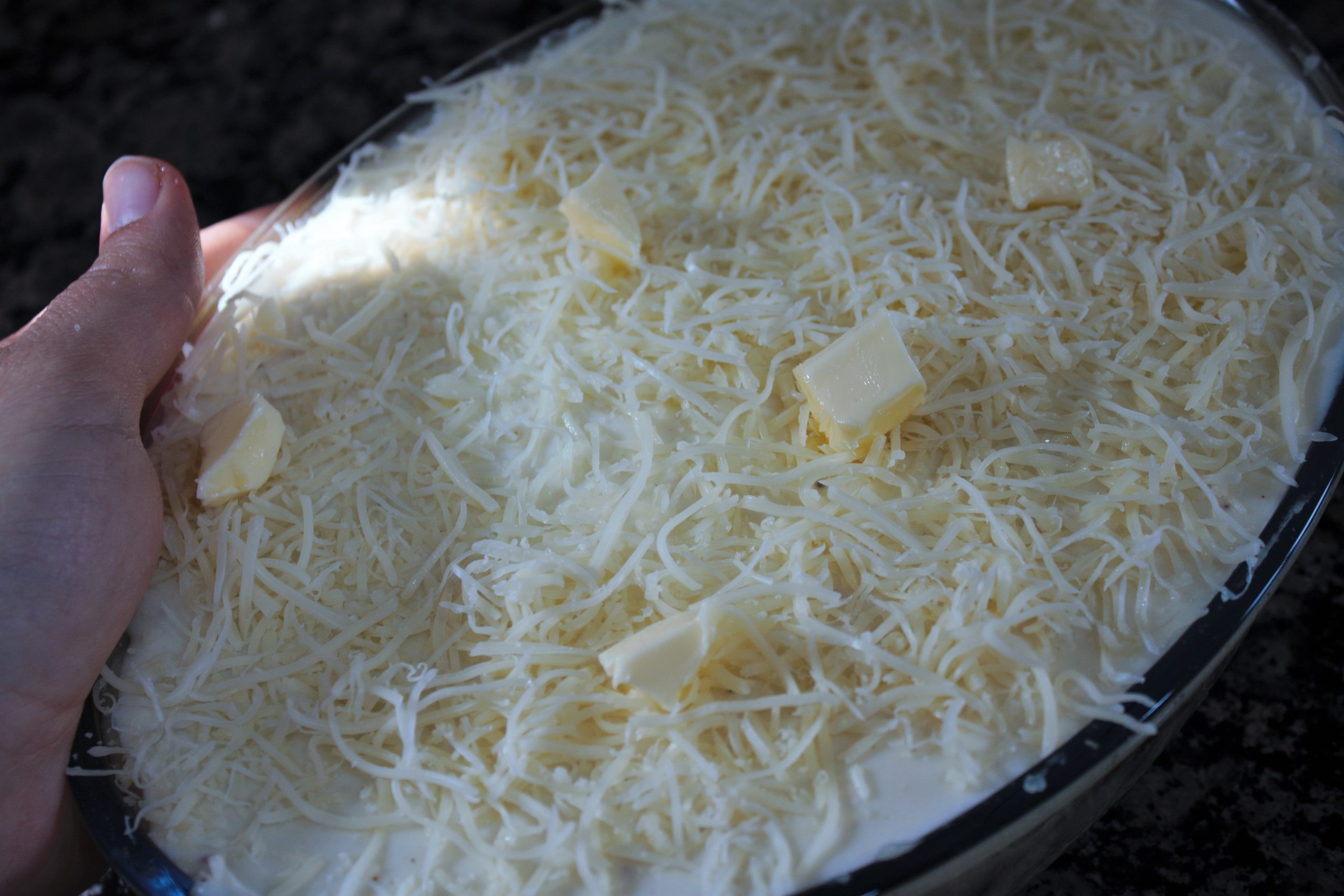Capa de bechamel y queso emmental rallado sobre pastel de patata antes de hornear