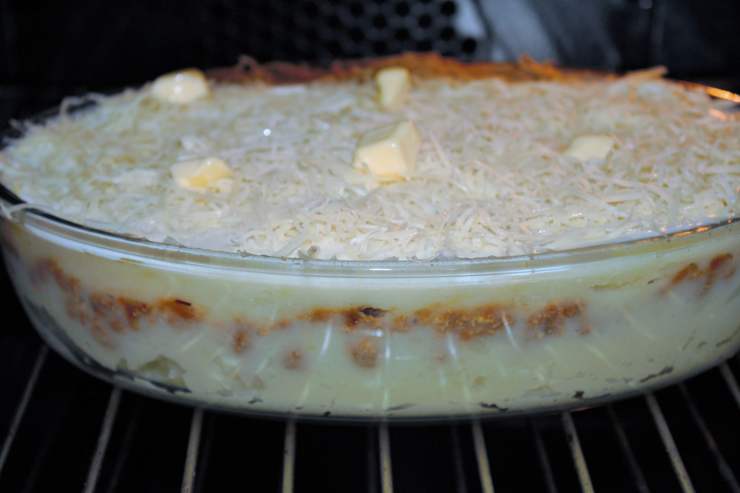 Capa de bechamel y queso emmental rallado sobre pastel de patata en el horno antes de gratinarlo.