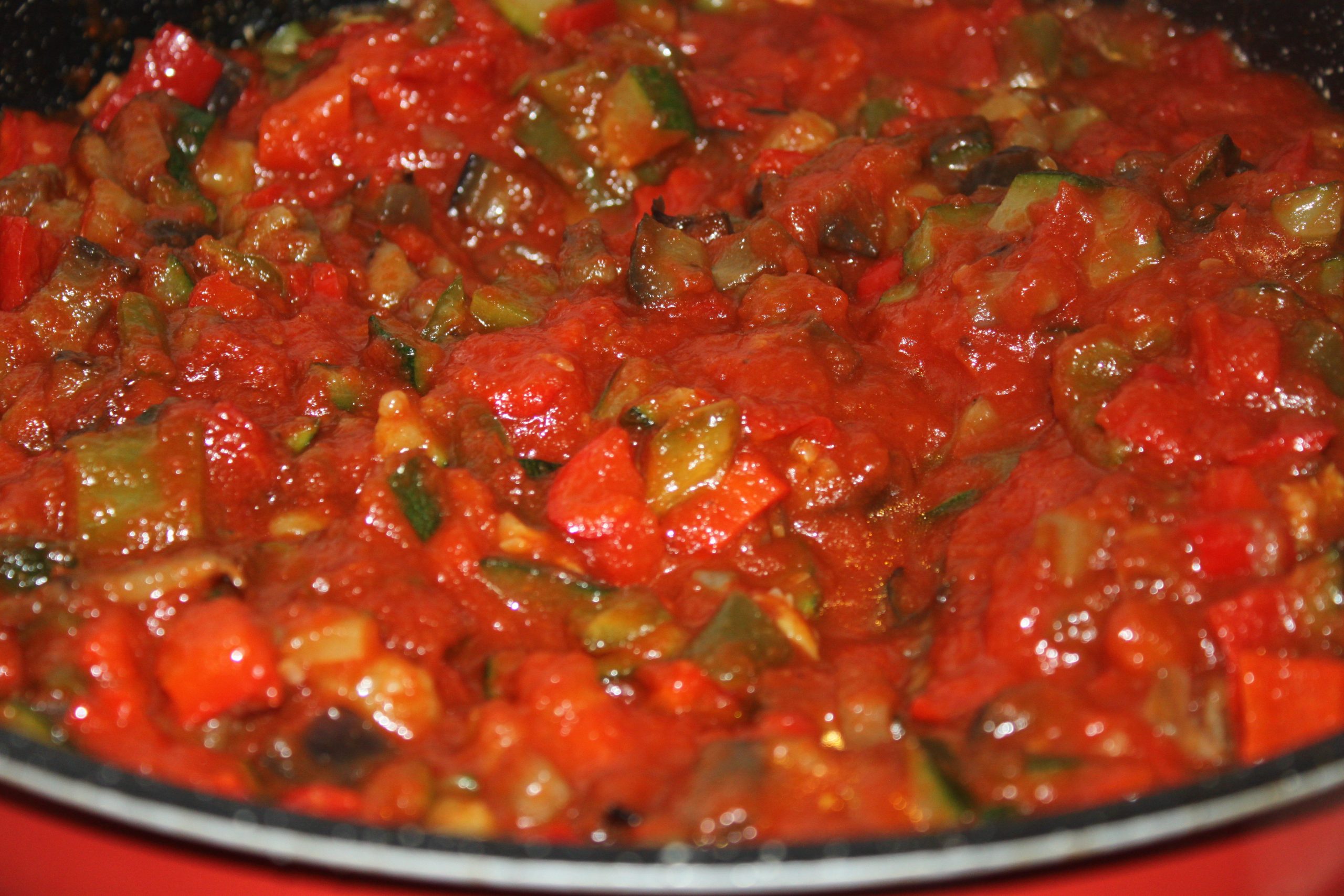 Cazuela de barro mezclando todas las verduras fritas con el tomate y el pavo.
