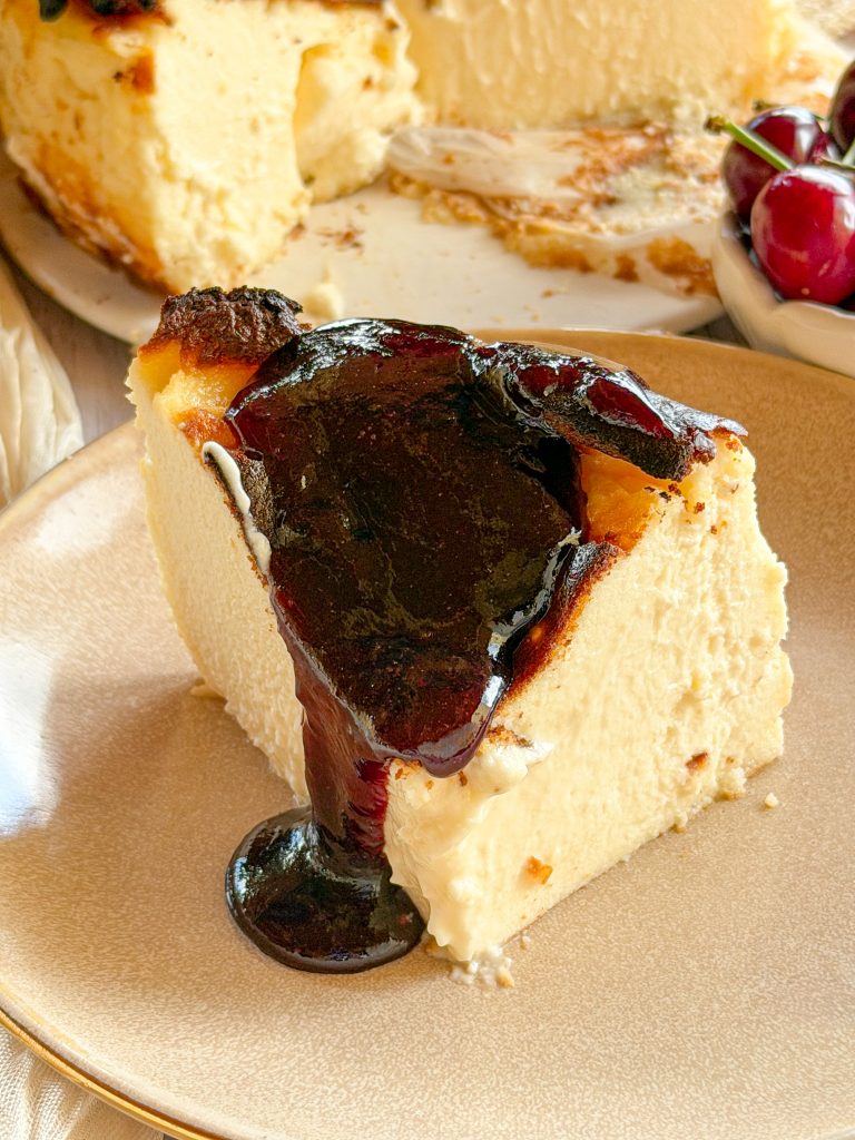 Primer plano cenital de una tarta de queso estilo La Viña con el centro fundente, mientras se vierte una mermelada casera de cerezas brillantes y trozos enteros de fruta sobre su superficie tostada