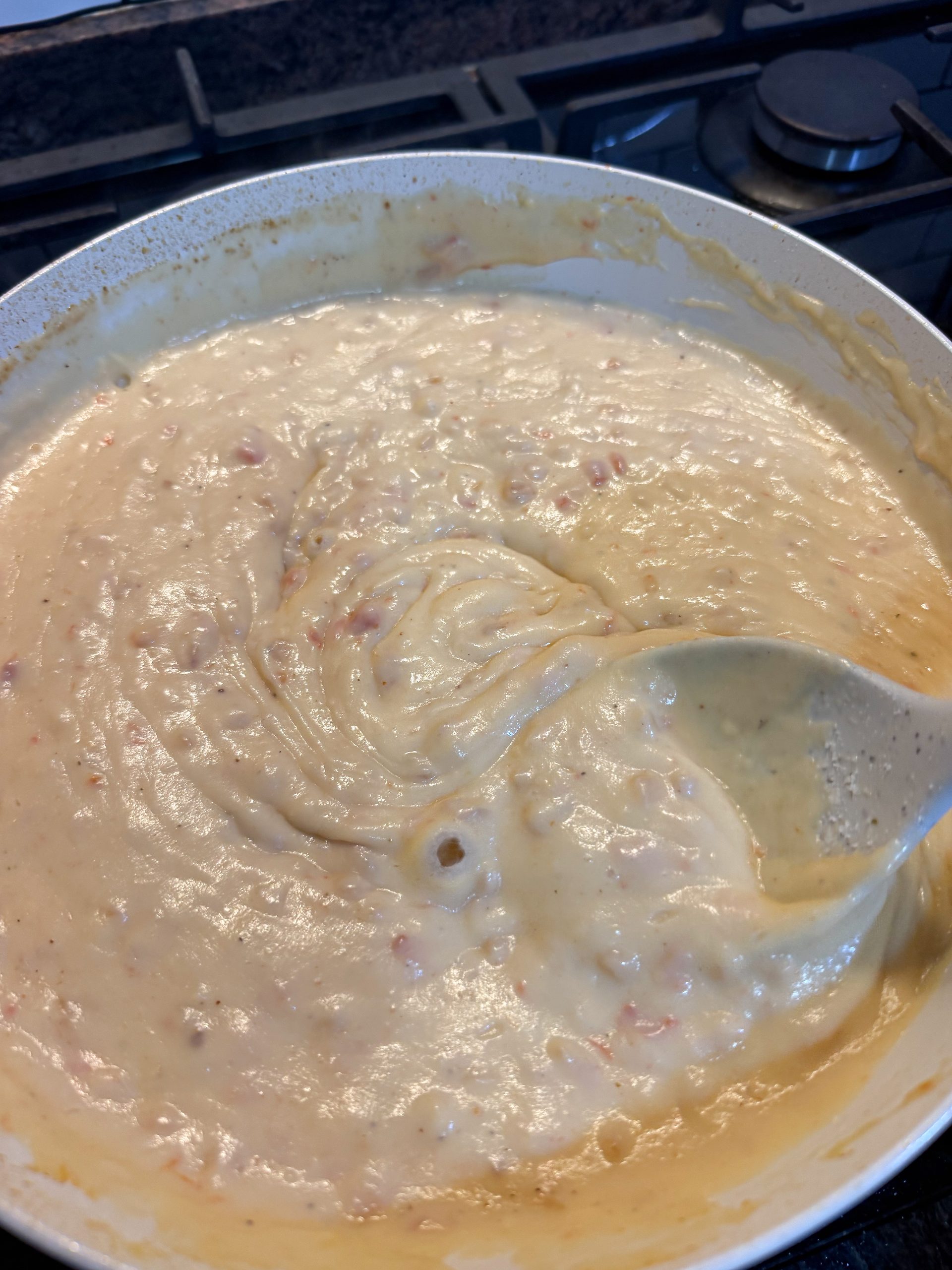 Bechamel cremosa cocinándose en la sartén, removida constantemente hasta obtener una textura suave y sin grumos.