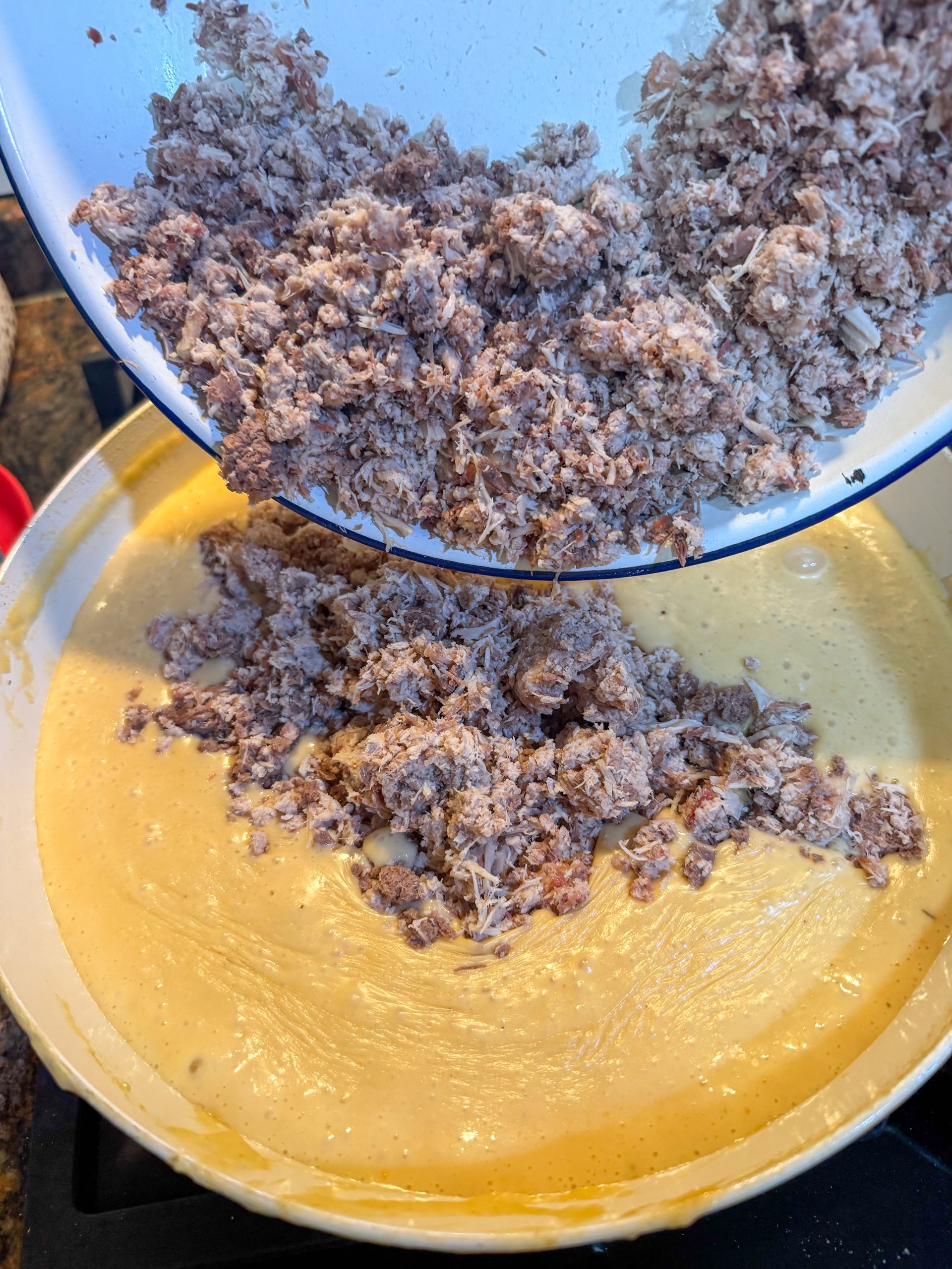 Carne del cocido desmenuzada incorporándose a la bechamel para preparar el relleno de las croquetas caseras.