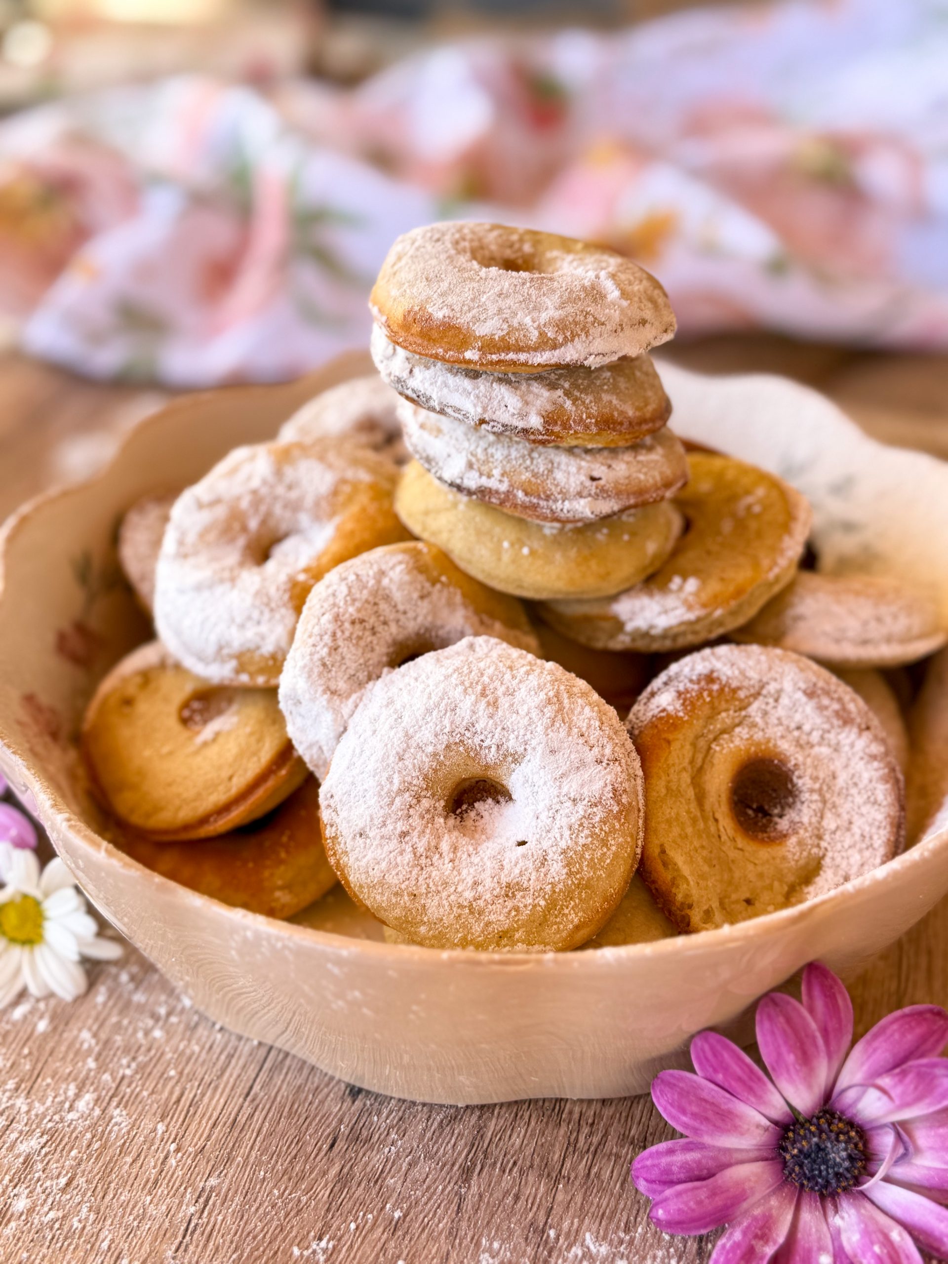 Torre de donetes caseros sabor cheesecake sin azúcar, espolvoreados con azúcar glas y decorados con flores blancas y lilas.
