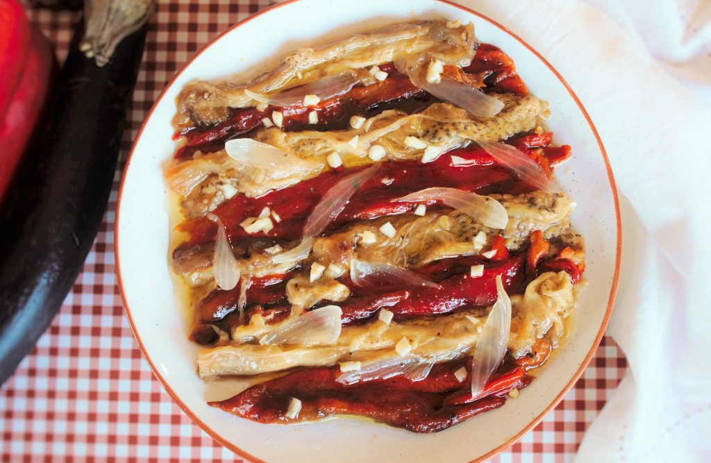 Escalivada a la brasa sobre plato rustico decorada con ajo picado y aceite de Oliva virgen extra.