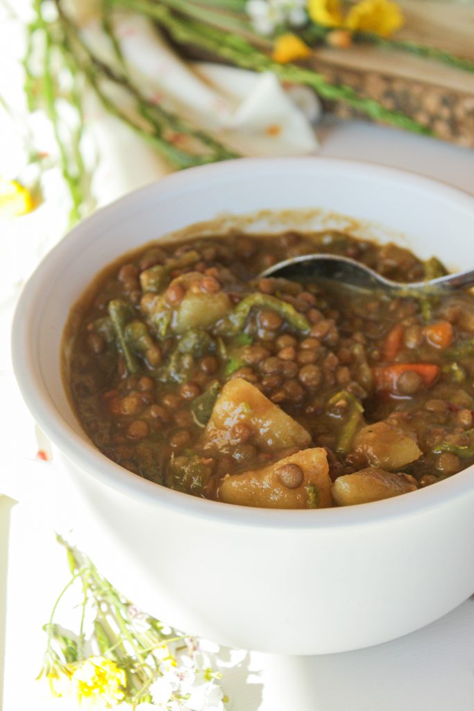 Cazuela de lentejas caseras de la abuela con esp&aacute;rragos trigueros silvestres, servidas en un cuenco de cer&aacute;mica r&uacute;stica con una ramita de tomillo fresco.