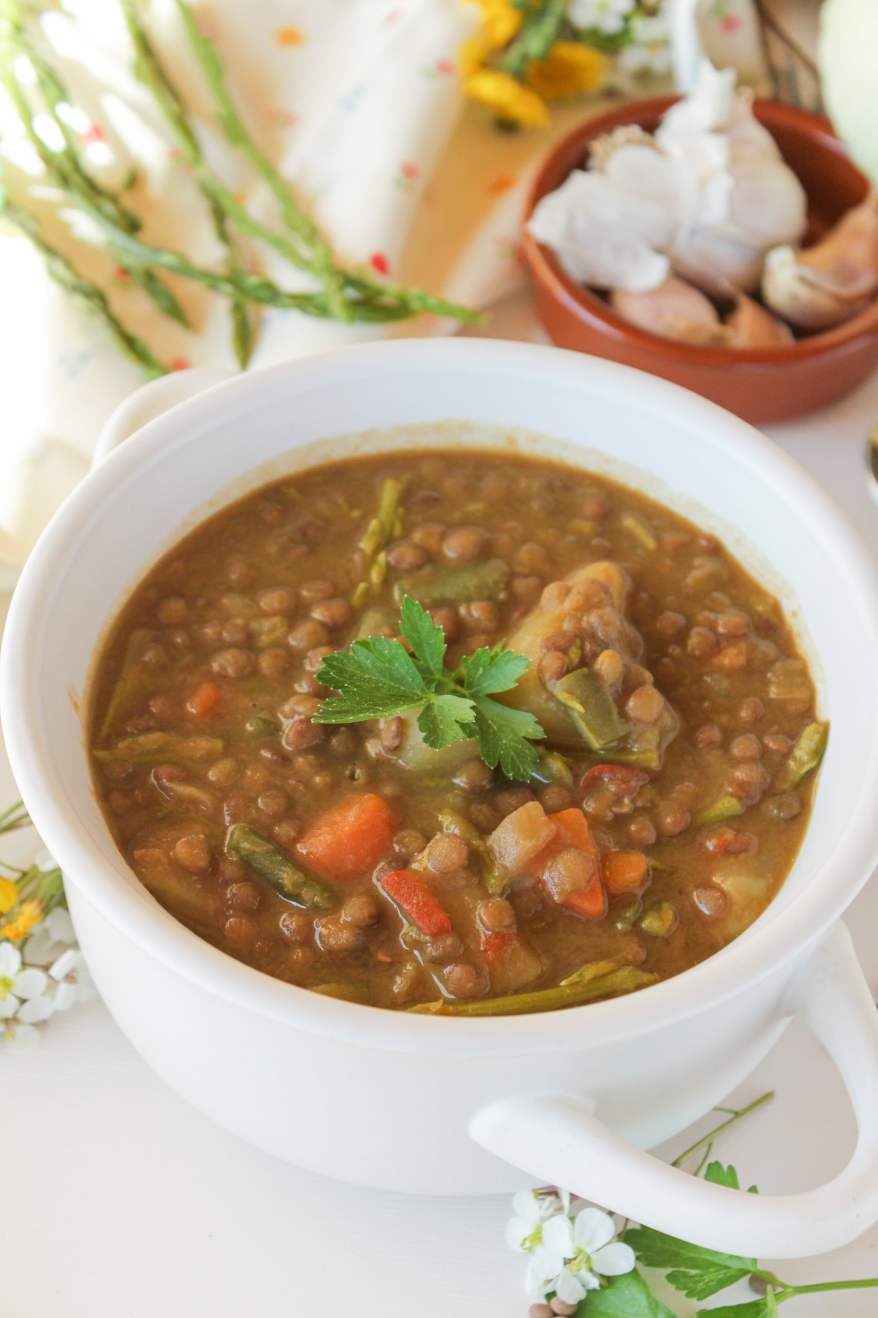 Cazuela de lentejas caseras de la abuela con esp&aacute;rragos trigueros silvestres, servidas en un cuenco de cer&aacute;mica r&uacute;stica con una ramita de tomillo fresco.