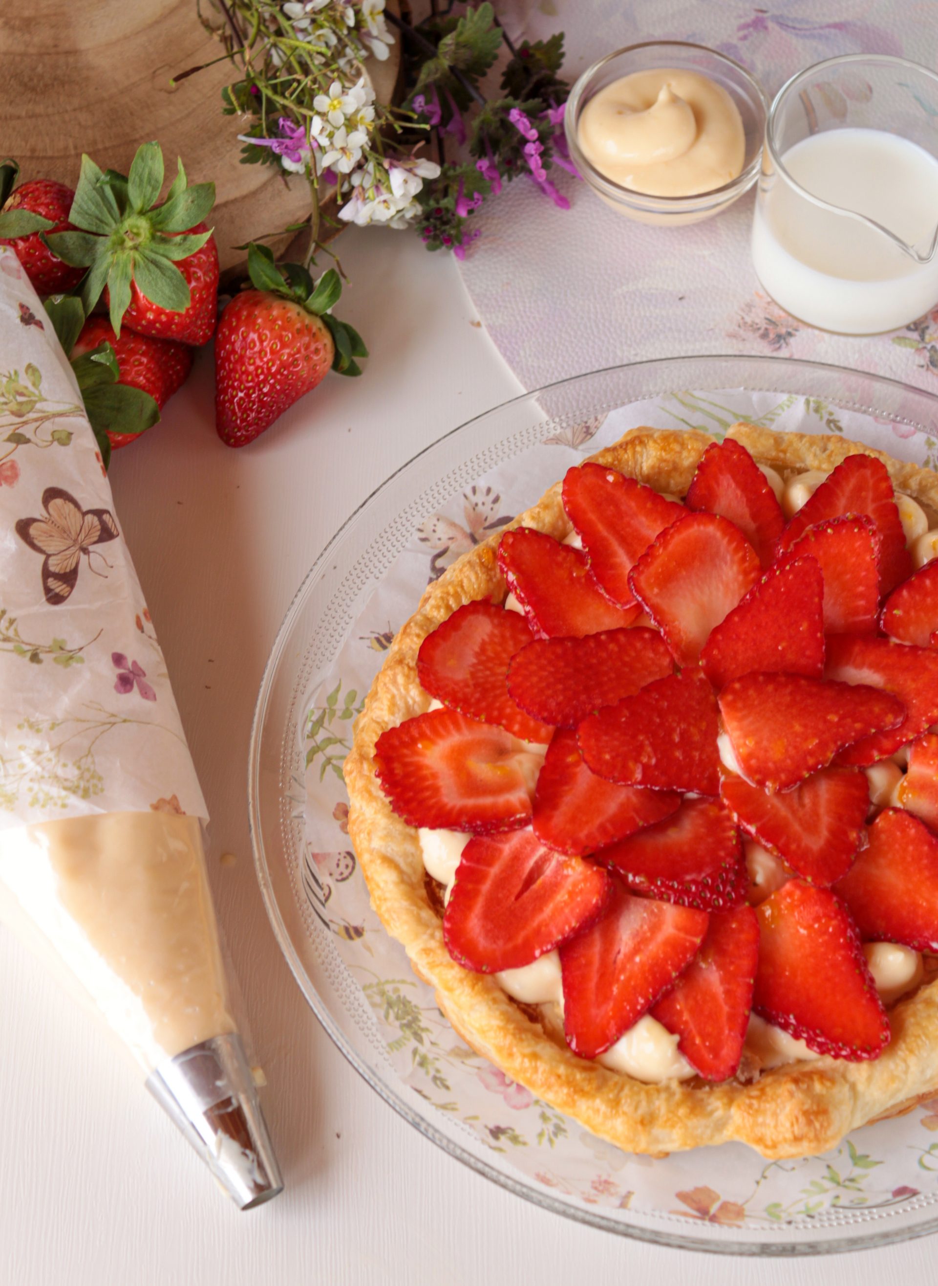 Tarta rectangular de hojaldre crujiente cubierta con una capa generosa de crema pastelera y filas ordenadas de fresas frescas brillantes, dispuesta sobre un papel de horno en una cocina rústica.