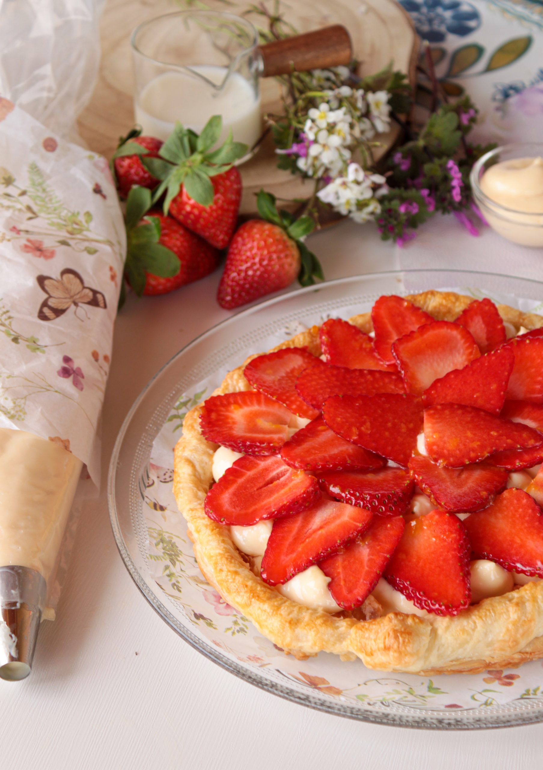 Tarta rectangular de hojaldre crujiente cubierta con una capa generosa de crema pastelera y filas ordenadas de fresas frescas brillantes, dispuesta sobre un papel de horno en una cocina rústica.