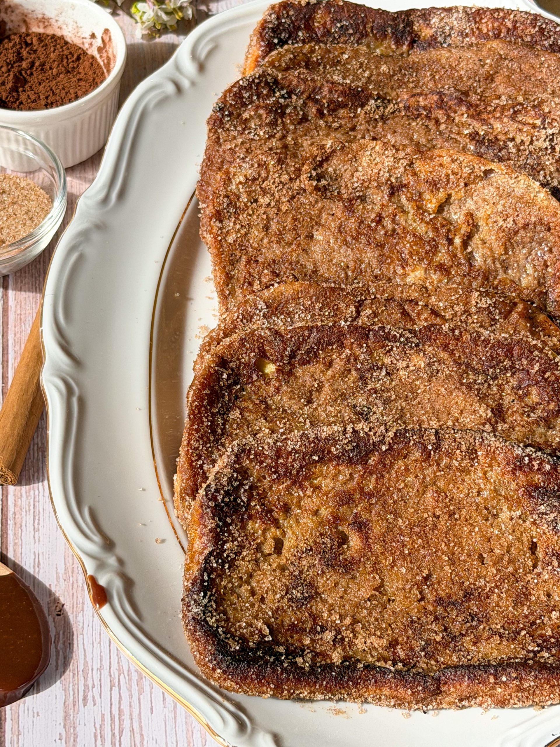 Plato de torrijas tradicionales de leche y canela espolvoreadas con azúcar sobre una mesa de madera.
