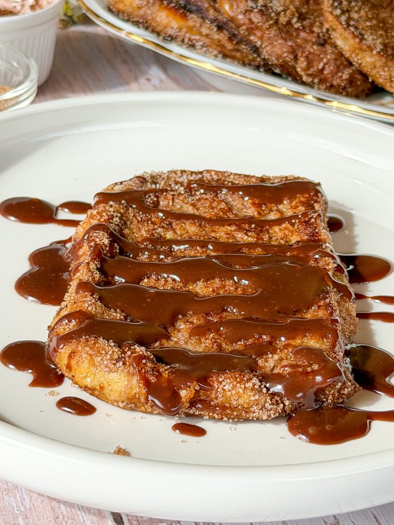 Un hilo de chocolate con leche derretido cayendo sobre una torrija de brioche y cacao espolvoreada con azúcar y canela.