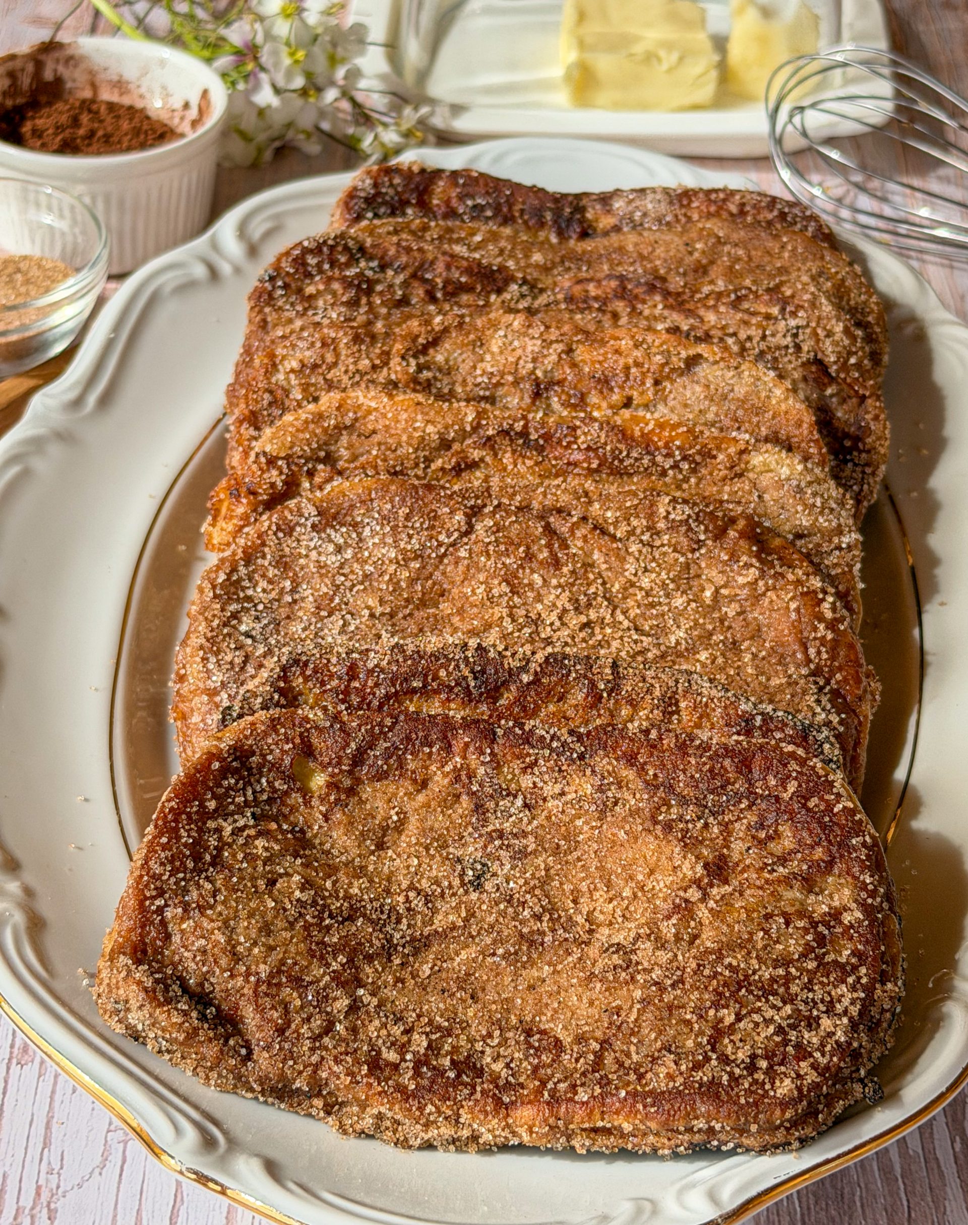Plato de torrijas tradicionales de leche y canela espolvoreadas con azúcar sobre una mesa de madera.