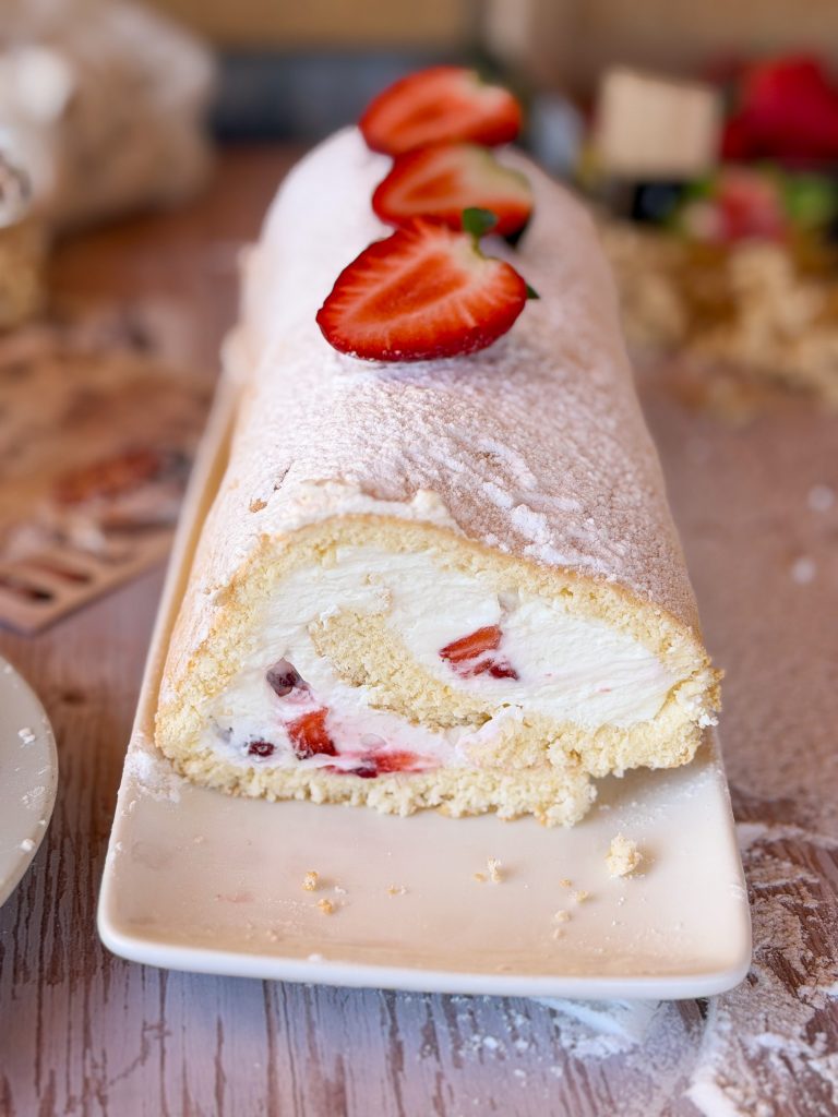 Primer plano de un bizcocho enrollado relleno de nata firme y trozos de fresas frescas naturales.