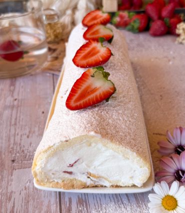 Primer plano de un bizcocho enrollado relleno de nata firme y trozos de fresas frescas naturales.
