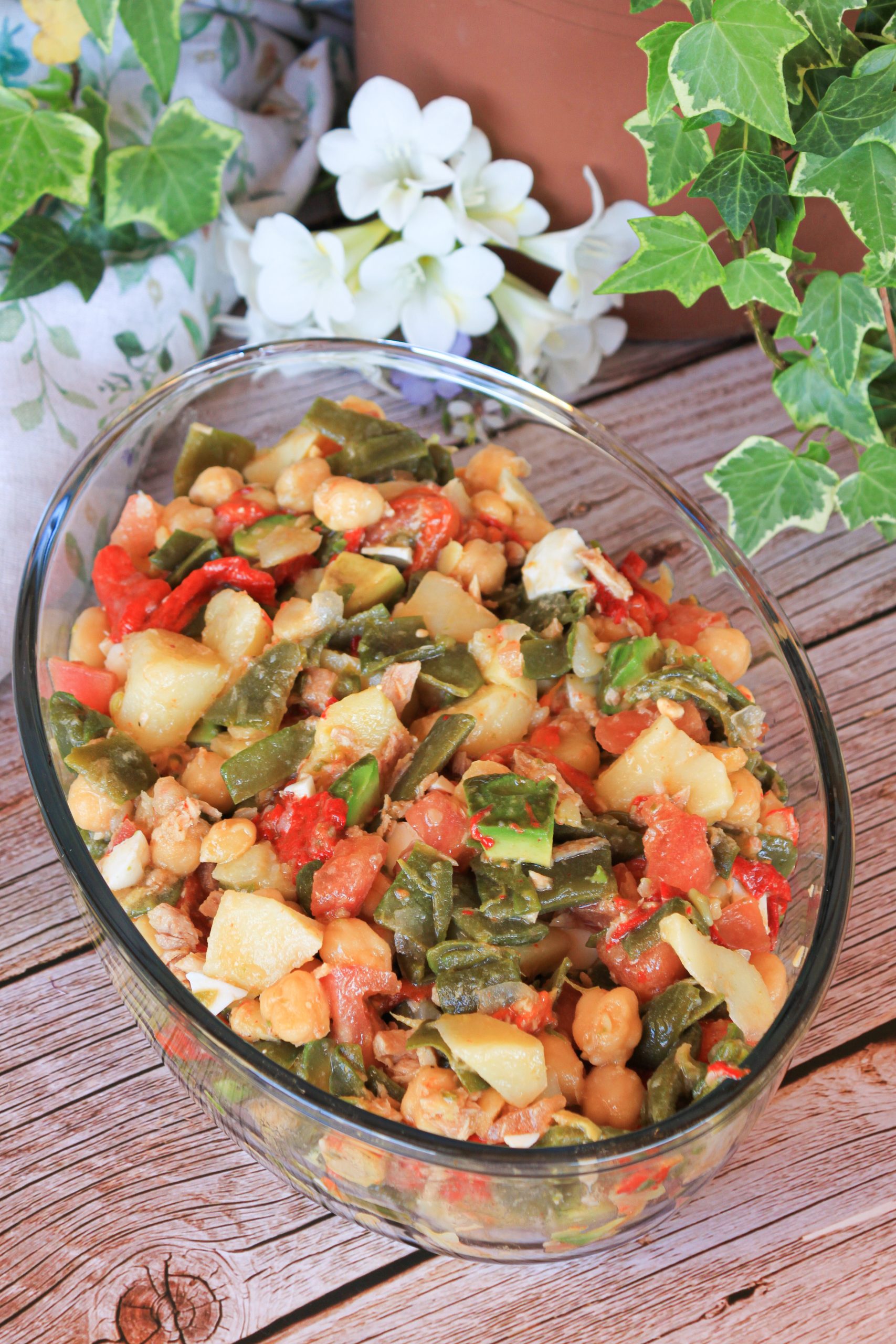 Primer plano de un bol de cer&aacute;mica con ensalada de jud&iacute;as verdes, patatas troceadas, garbanzos, aguacate y huevo cocido, con un ali&ntilde;o brillante de aceite de oliva sobre una mesa de madera r&uacute;stica.