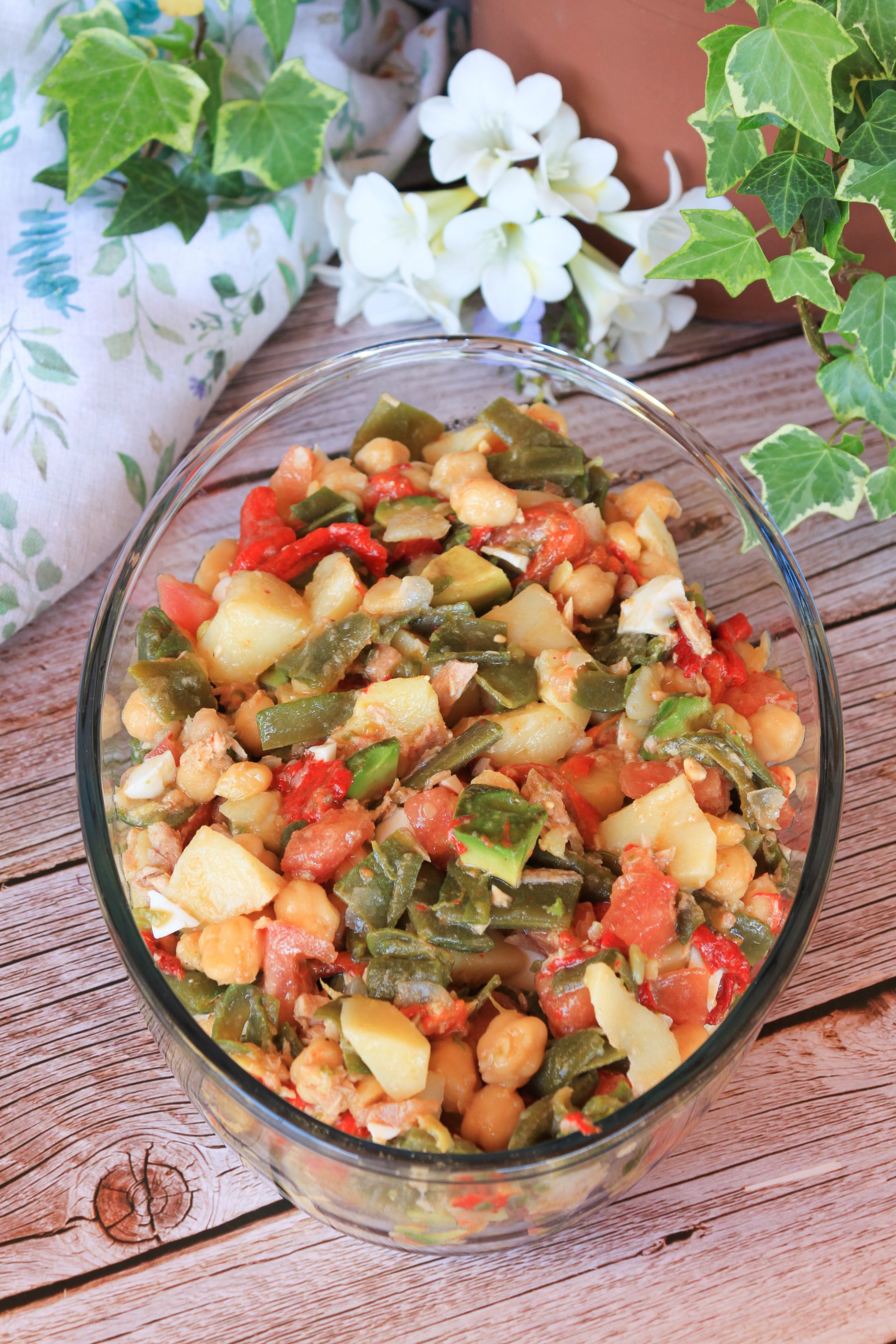 Primer plano de un bol de cerámica con ensalada de judías verdes, patatas troceadas, garbanzos, aguacate y huevo cocido, con un aliño brillante de aceite de oliva sobre una mesa de madera rústica.