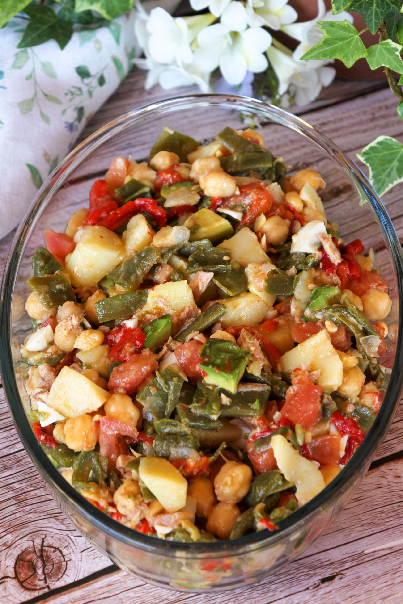 Primer plano de un bol de cerámica con ensalada de judías verdes, patatas troceadas, garbanzos, aguacate y huevo cocido, con un aliño brillante de aceite de oliva sobre una mesa de madera rústica.