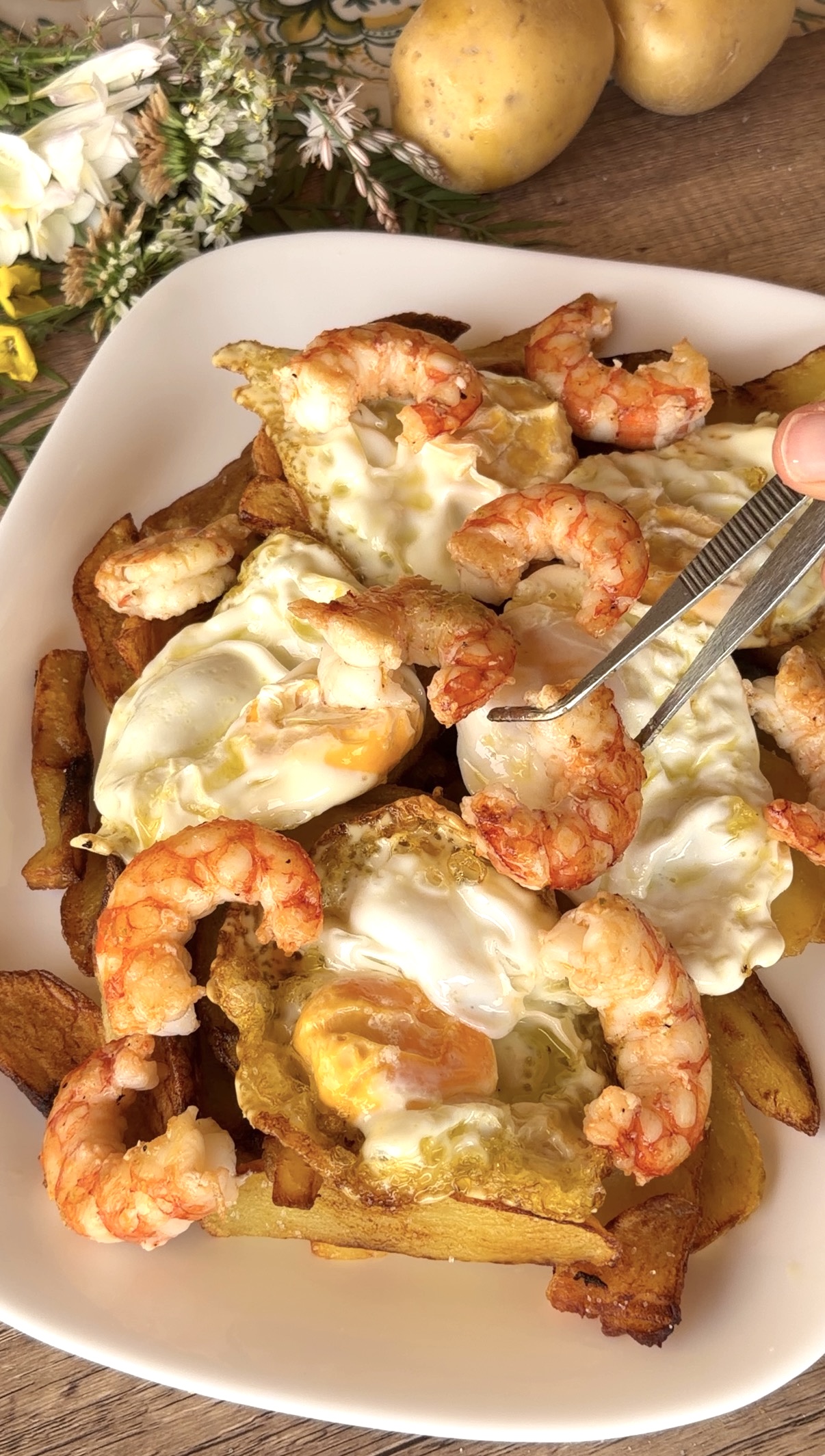 Sirviendo los gambones con unas pinzas sobre la cama de huevos fritos y patatas
