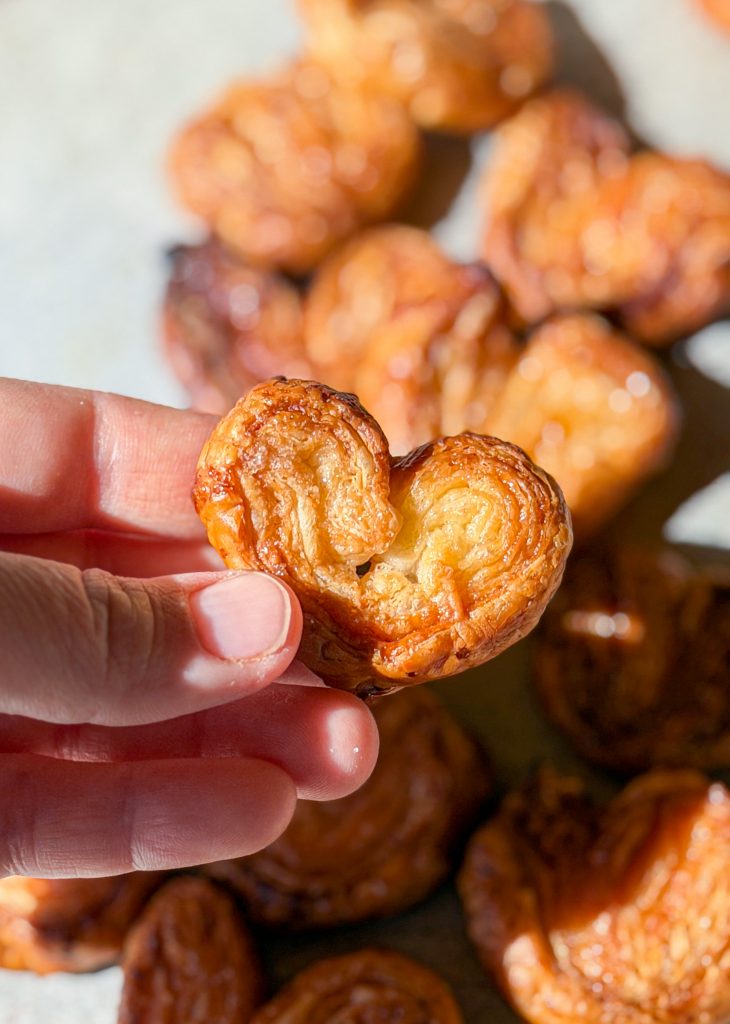 Palmeritas de hojaldre caseras muy doradas y caramelizadas con azúcar, dispuestas de forma estética sobre una superficie de madera rústica.