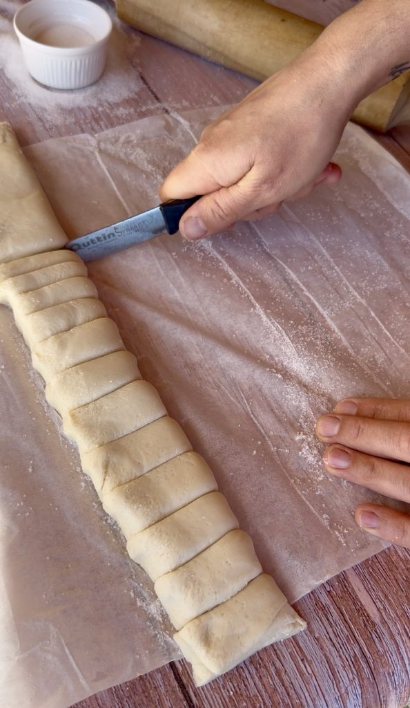 Lámina de hojaldre rectangular extendida sobre una superficie cubierta de azúcar blanco, lista para ser enrollada.