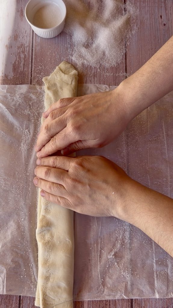 Lámina de hojaldre rectangular extendida sobre una superficie cubierta de azúcar blanco, lista para ser enrollada.